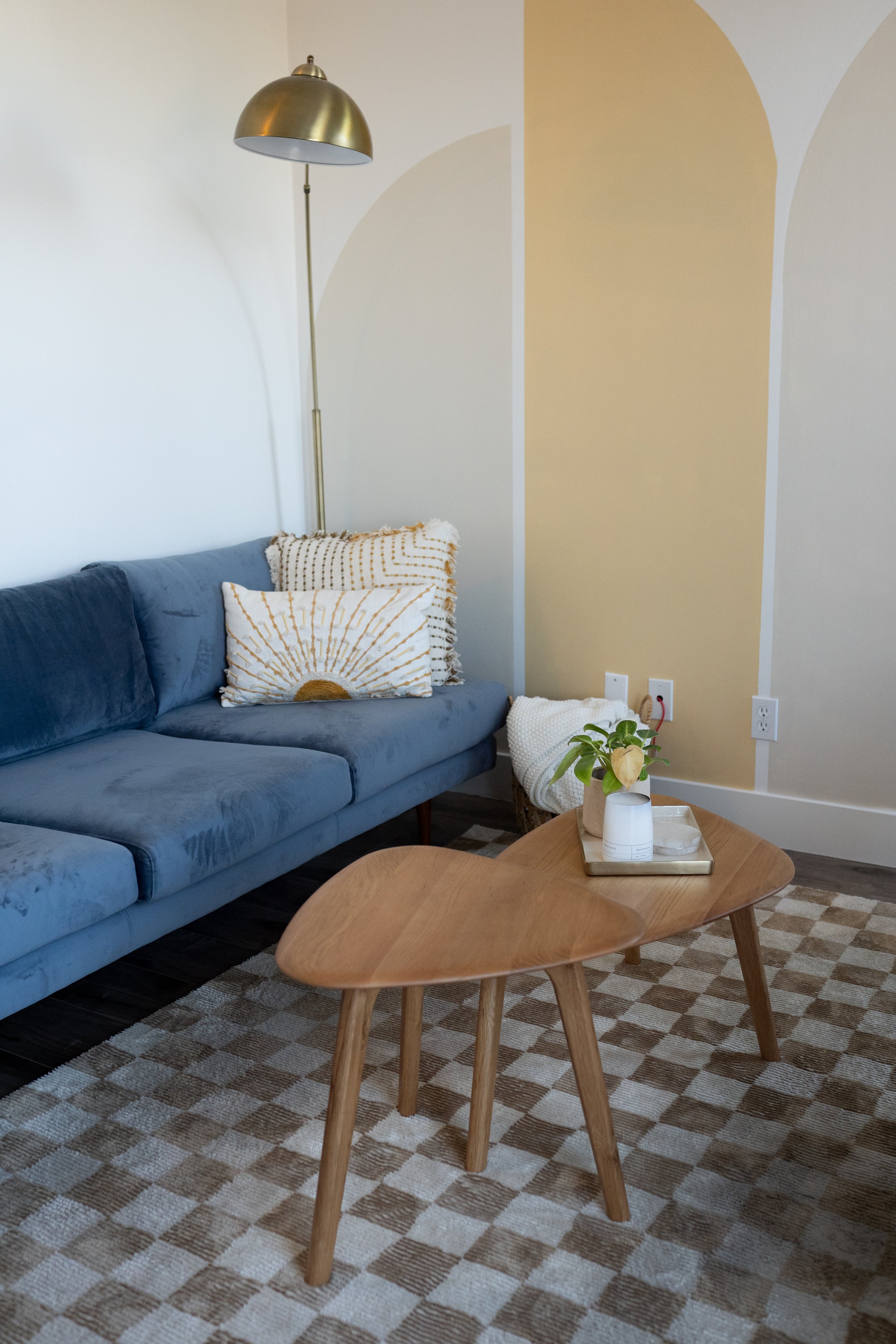 Living room with blue couch, wooden coffee table, striped pillows, beige and white wall, potted plant, and gold floor lamp.