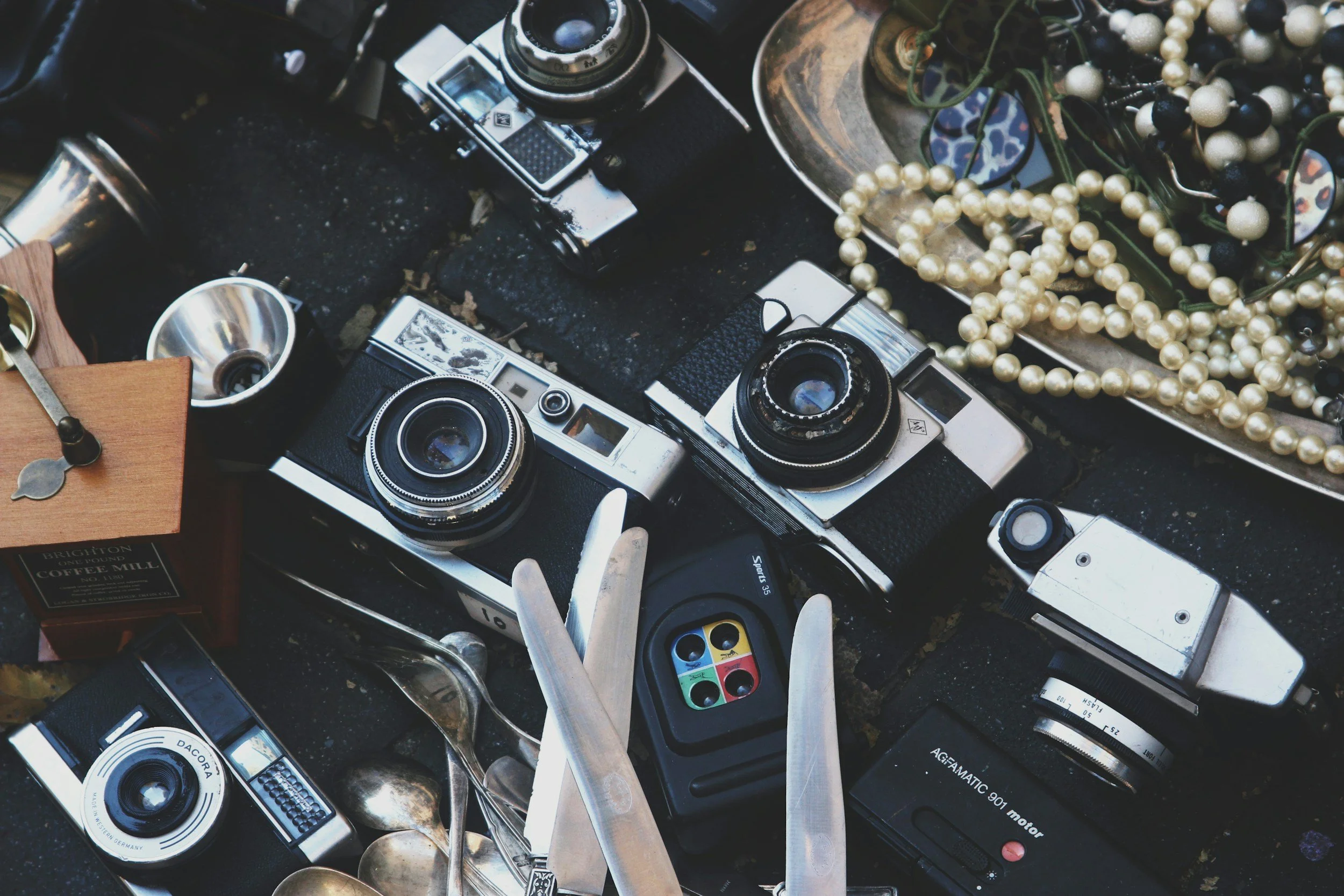 Vintage cameras, jewelry, and silverware on a table at a flea market or thrift sale.