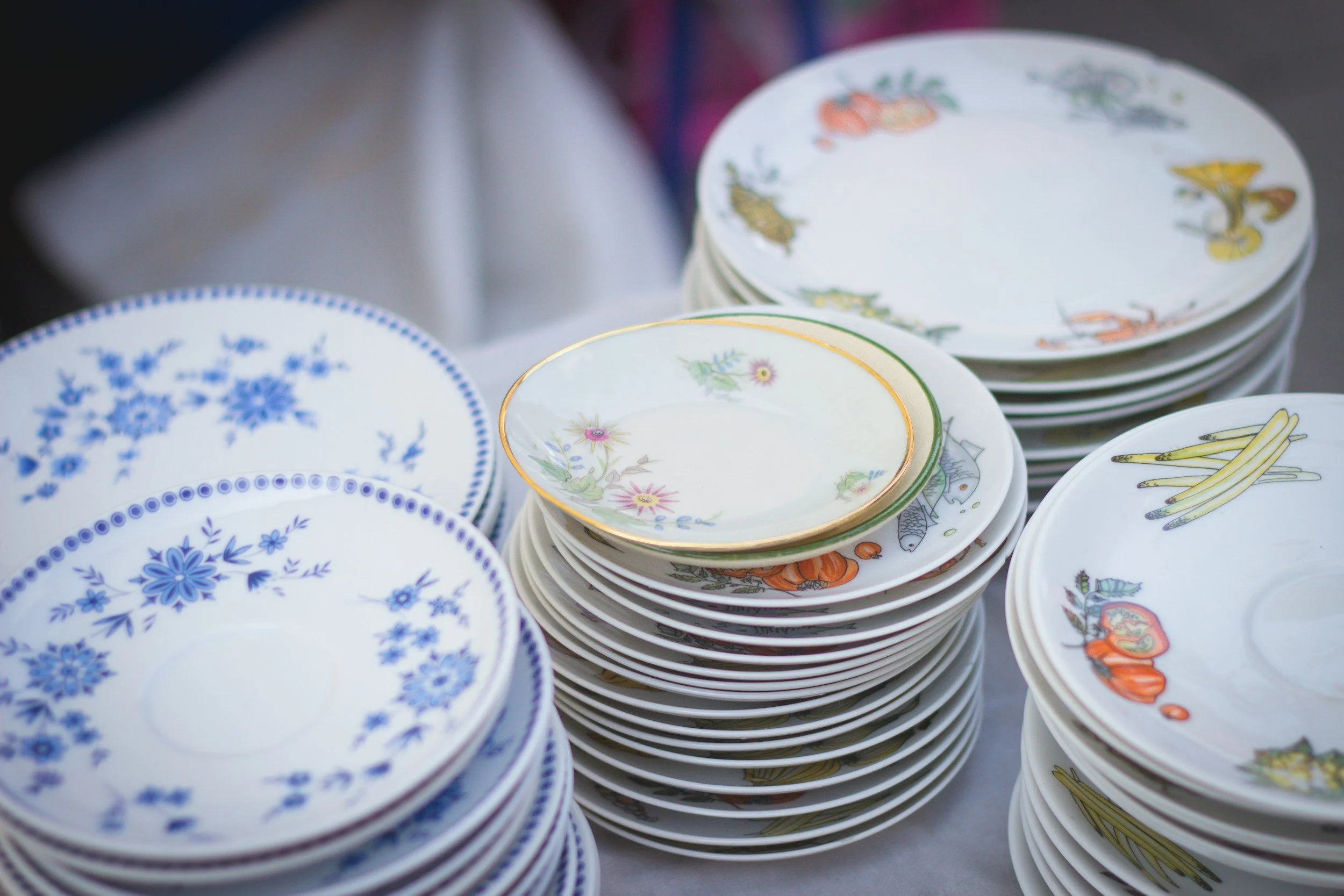 Stacks of decorative ceramic plates with floral and vegetable patterns.