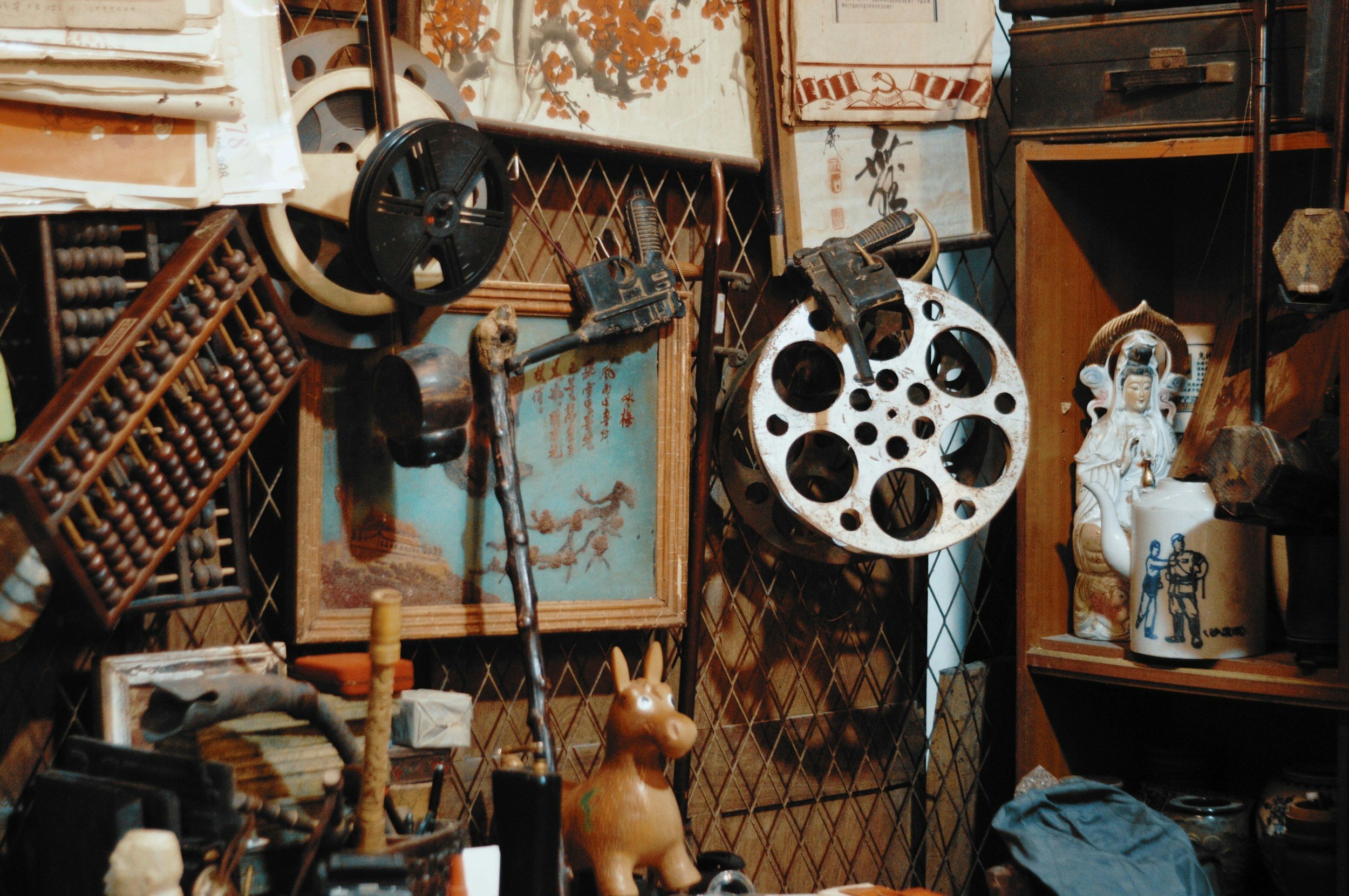 Vintage antique items and Asian decor on shelves and walls, including a large iron gear, framed artwork, a ceramic horse, and a porcelain statue.