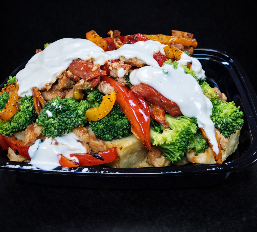 A black container filled with stir-fried vegetables including broccoli, red and yellow bell peppers, and squash, topped with white sauce.