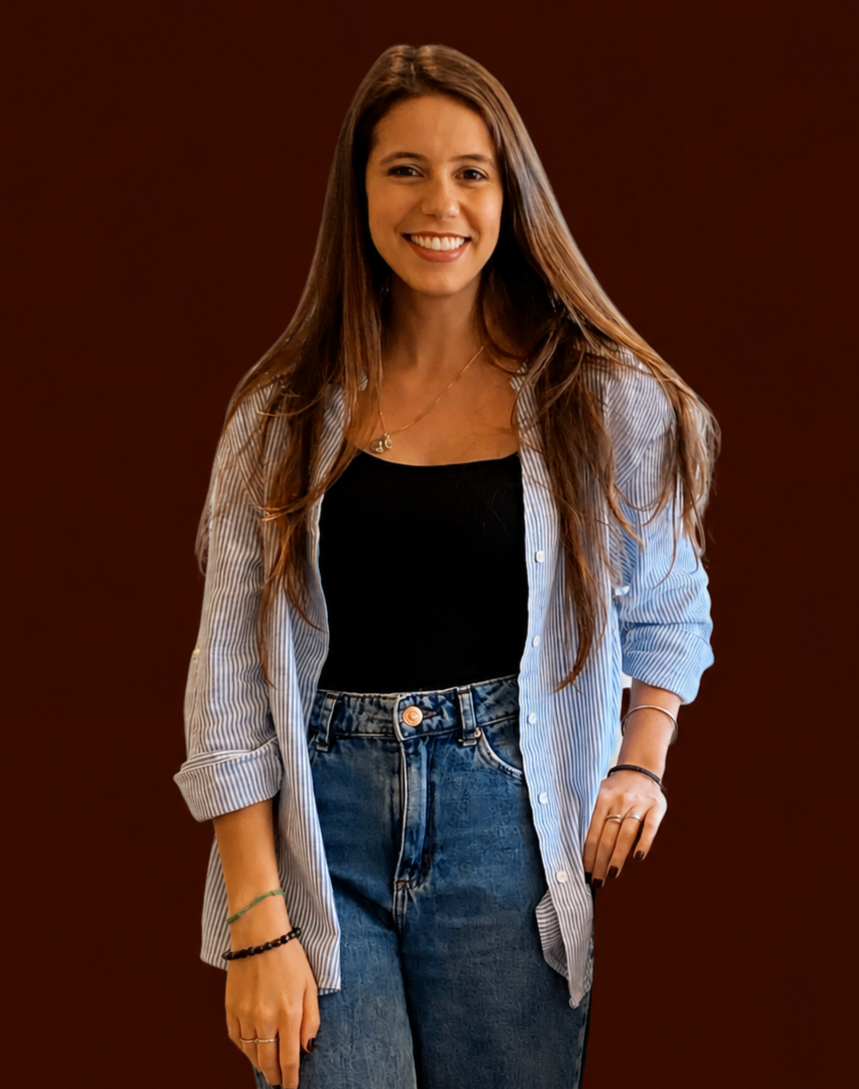 Young woman with long brown hair smiling, wearing a black top, a blue striped shirt open over it, and high-waisted jeans, standing against a brown background.