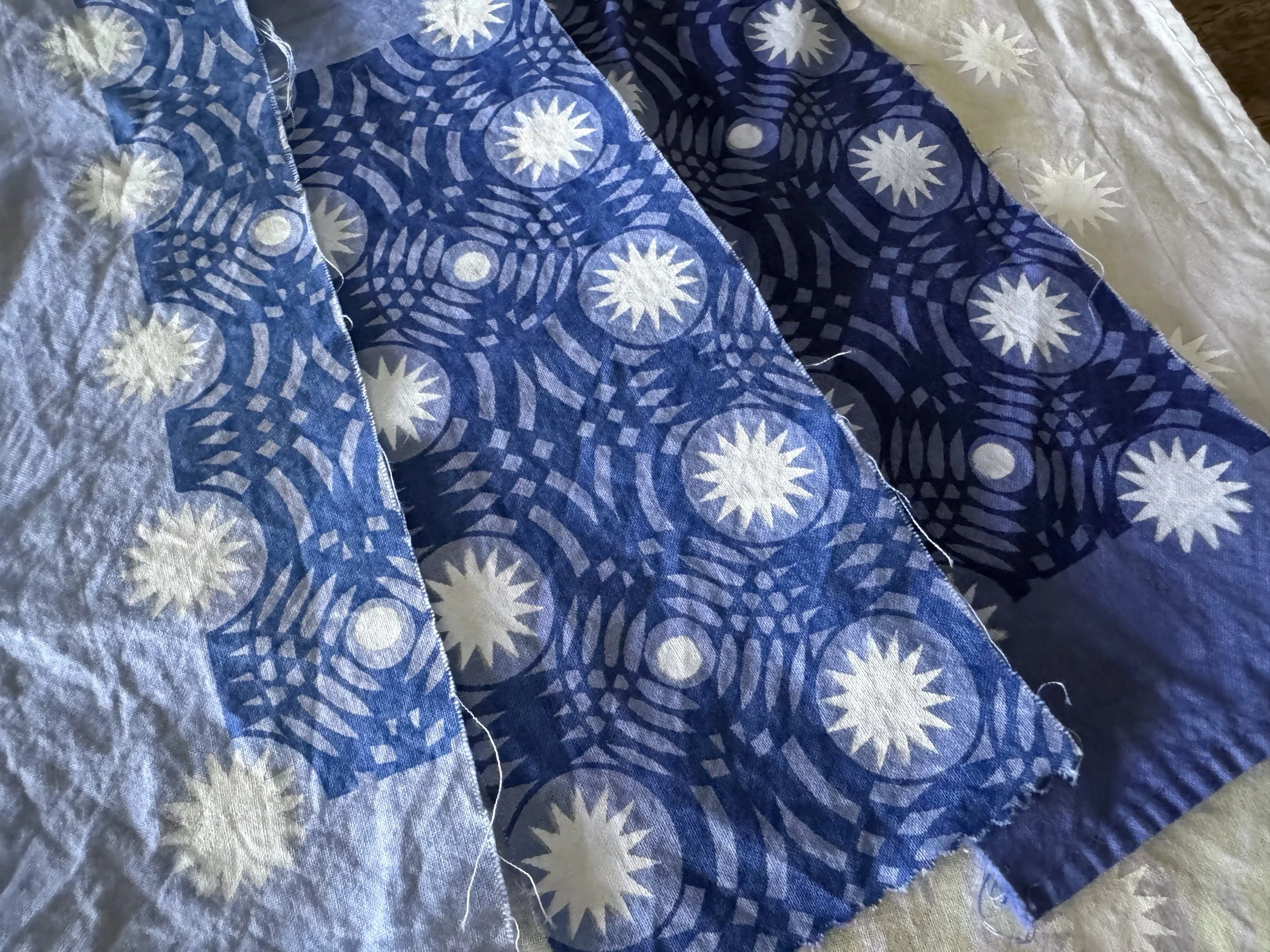 Close-up of three pieces of fabric with blue and white starburst circular patterns, overlapping each other, on a beige surface.