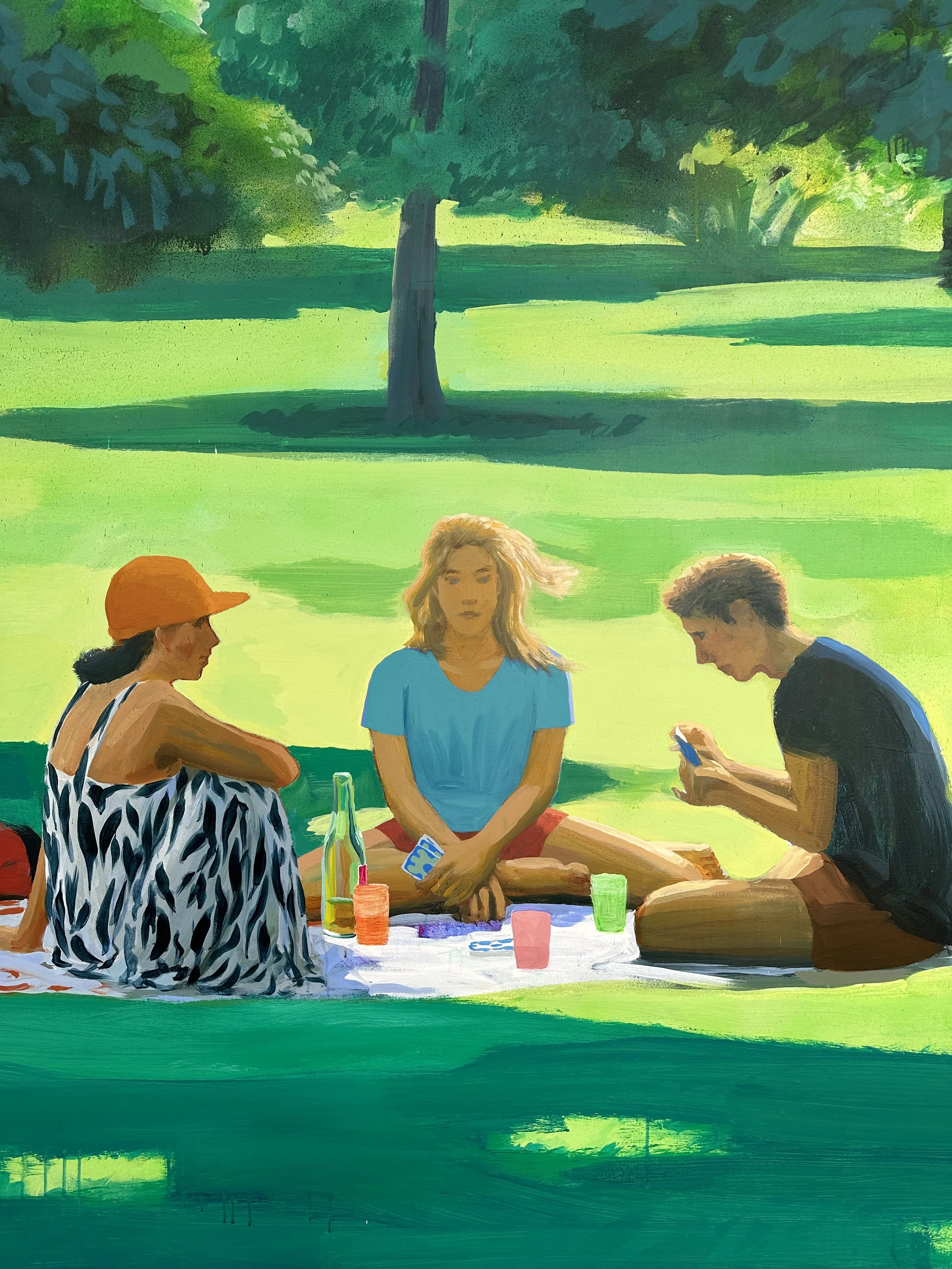 Three young people sitting on a blanket in a park with green grass and trees, two women and one man; the woman on the left is wearing an orange hat and a sleeveless animal print top, the woman in the middle has blonde hair and is wearing a blue T-shirt, and the man on the right has short hair and is wearing a black T-shirt, looking at his phone, with drinks and a bottle on the blanket.