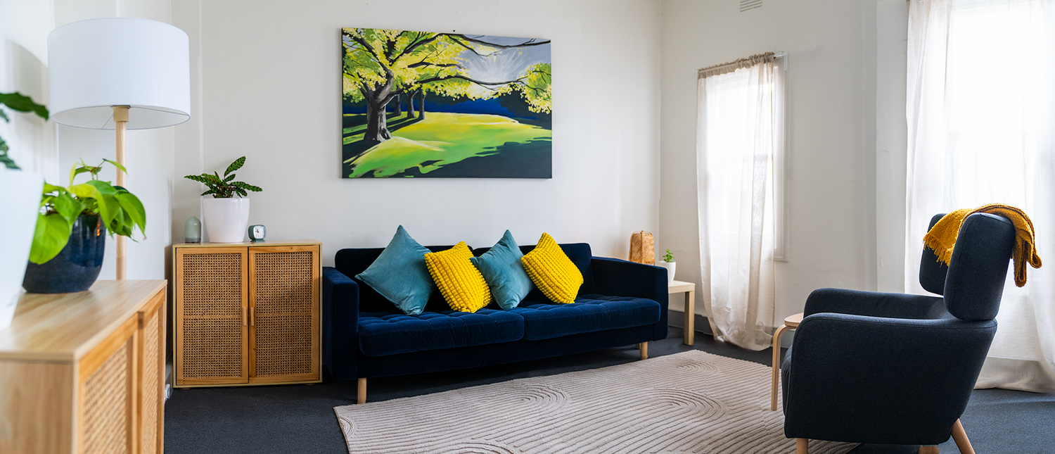 Consulting room with a blue sofa, yellow cushions and garden artwork.