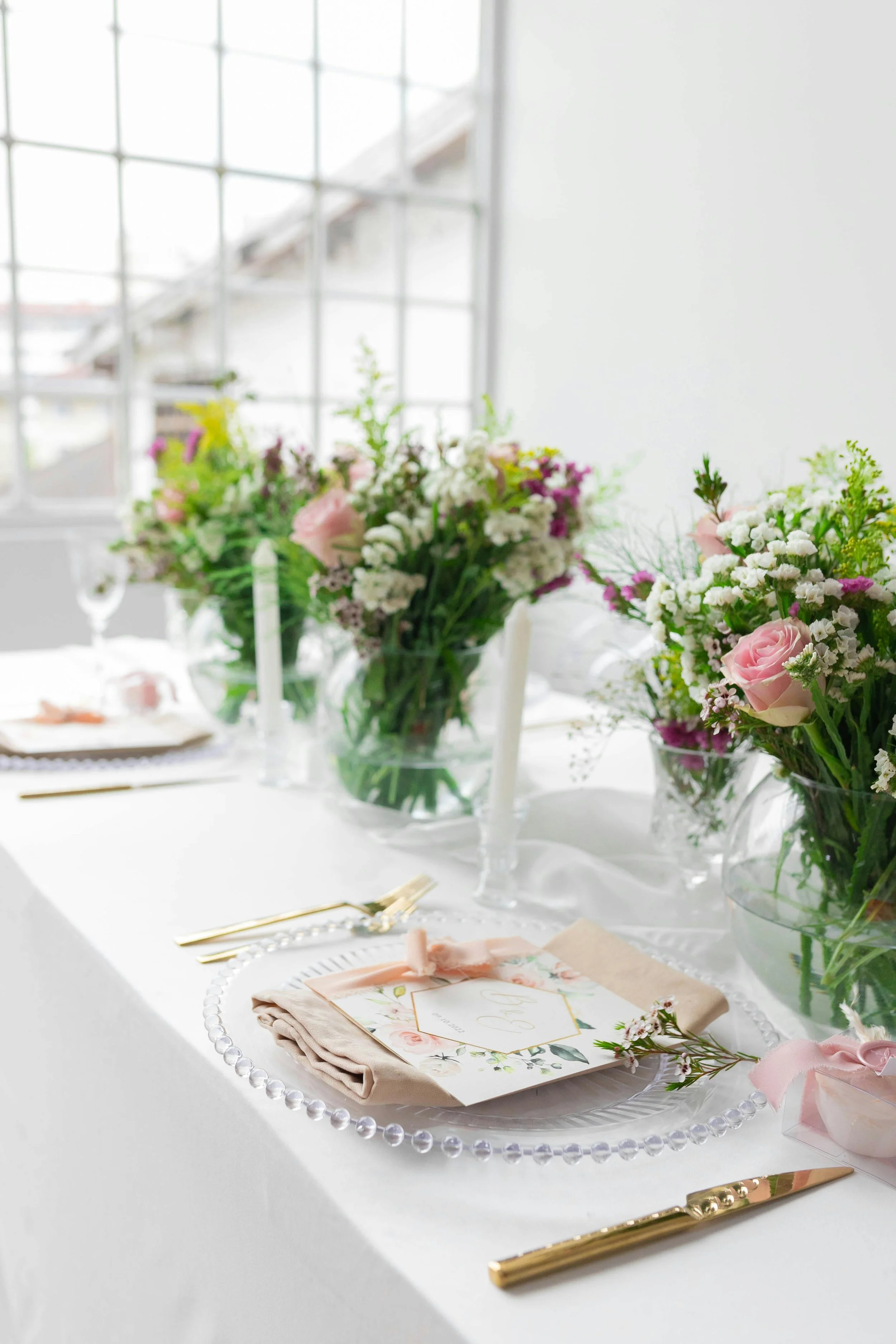 Elegant wedding table setting with floral centerpieces, candles, gold cutlery, and a printed menu on a white tablecloth.