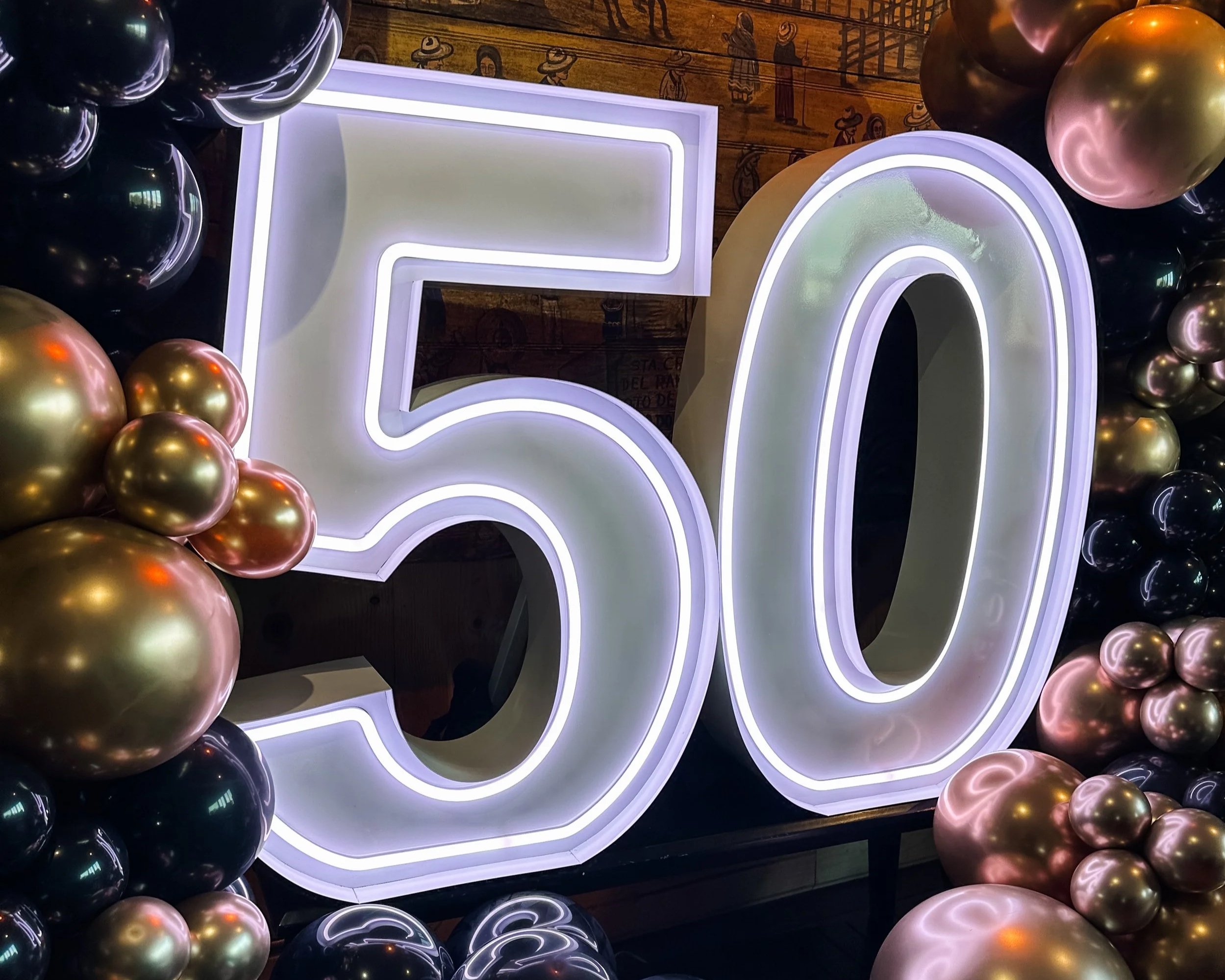 Large white illuminated number 50 decorated with black, gold, and pink balloons.