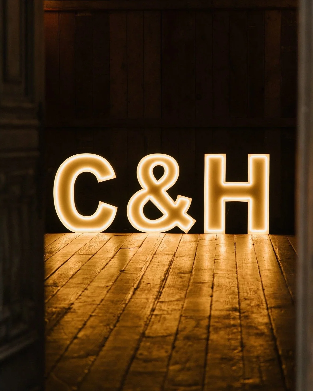 Backlit decorative letters spelling 'C & H' on wooden floor in dark, indoor setting.