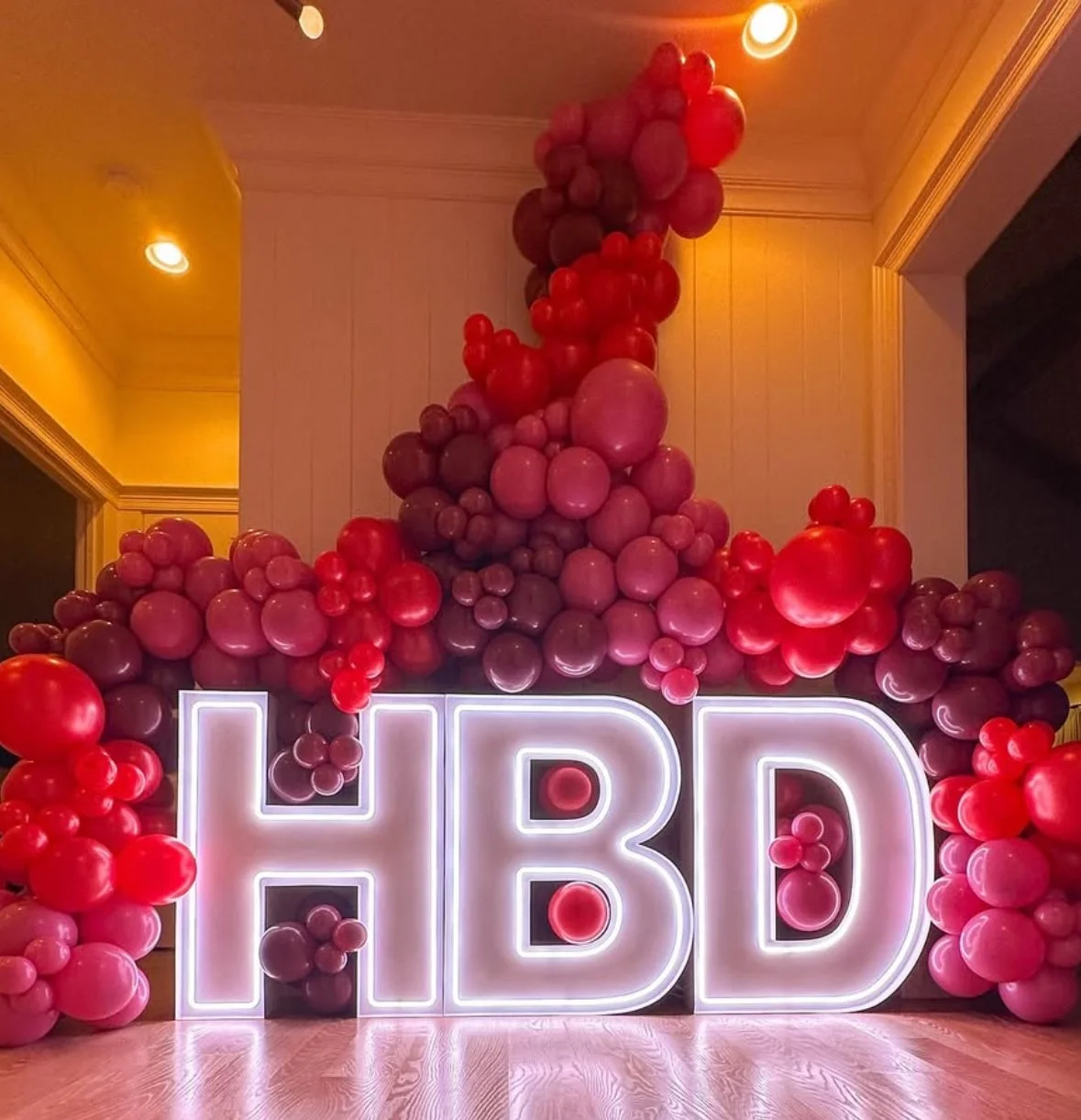 Decorative display with large illuminated letters 'HBD' surrounded by pink and red balloons.