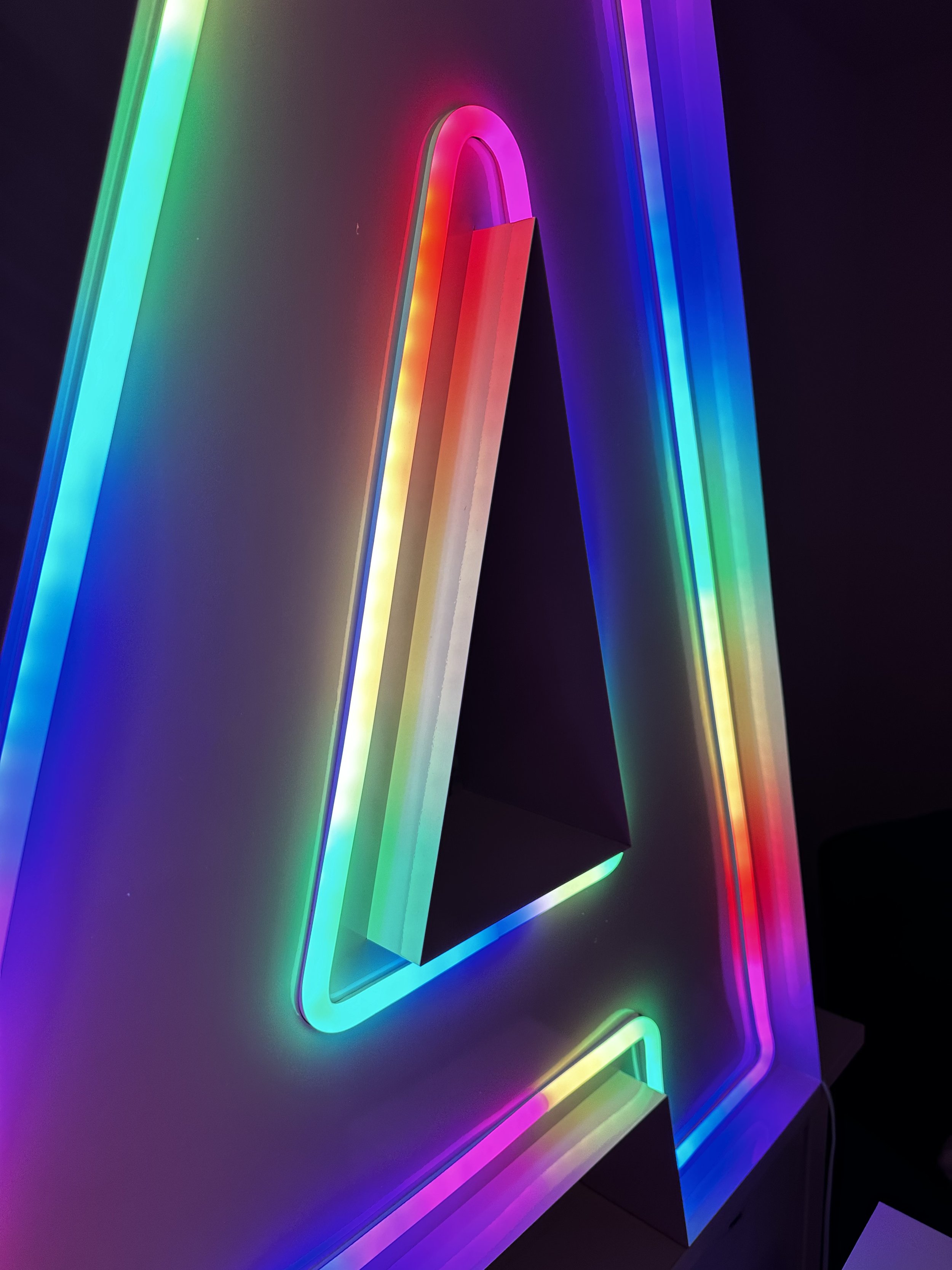 Colorful illuminated triangle with rainbow neon lights on a dark background.