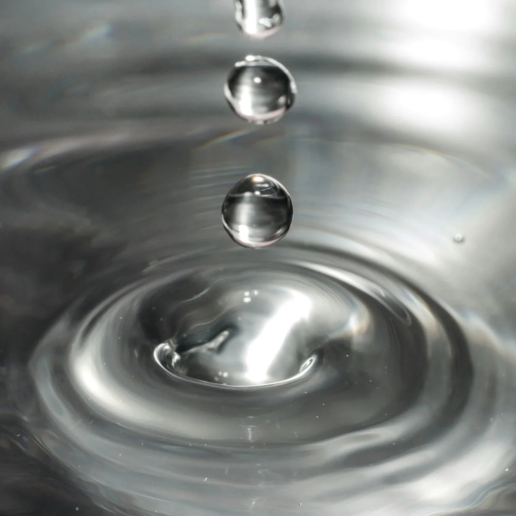 Close-up of water droplet falling into a body of water, creating ripples.