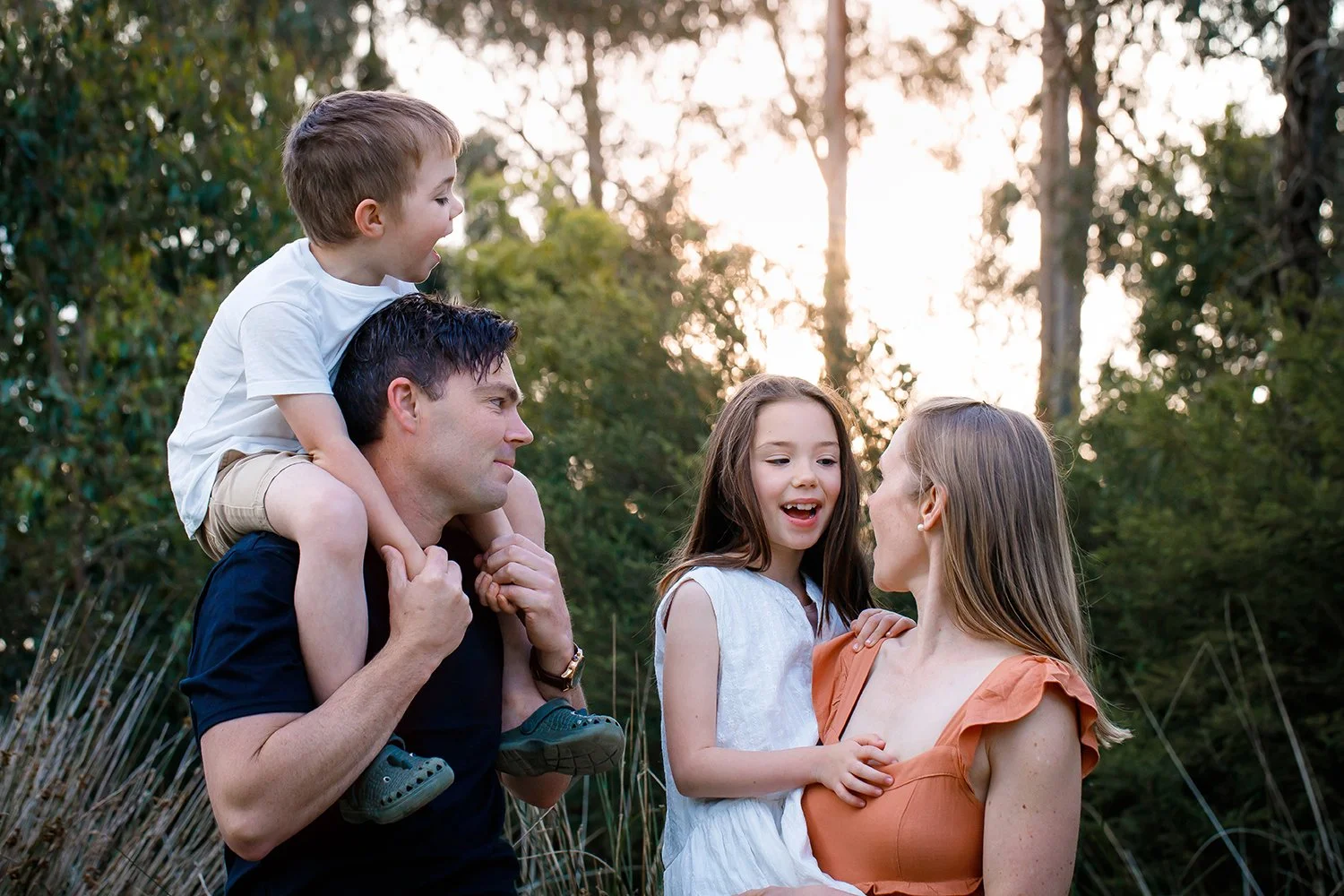 Family of four outdoors during sunset, parents with two children, one boy and one girl, smiling and interacting.