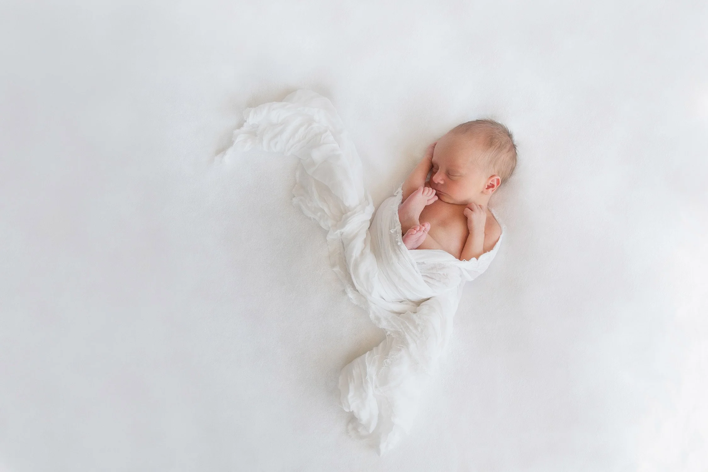 A newborn baby sleeping peacefully on a white blanket, wrapped in a white cloth.