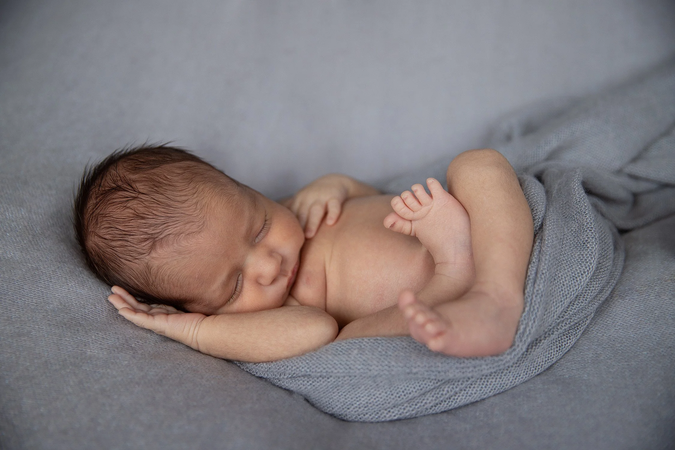 A sleeping newborn baby lying on a soft grey blanket.