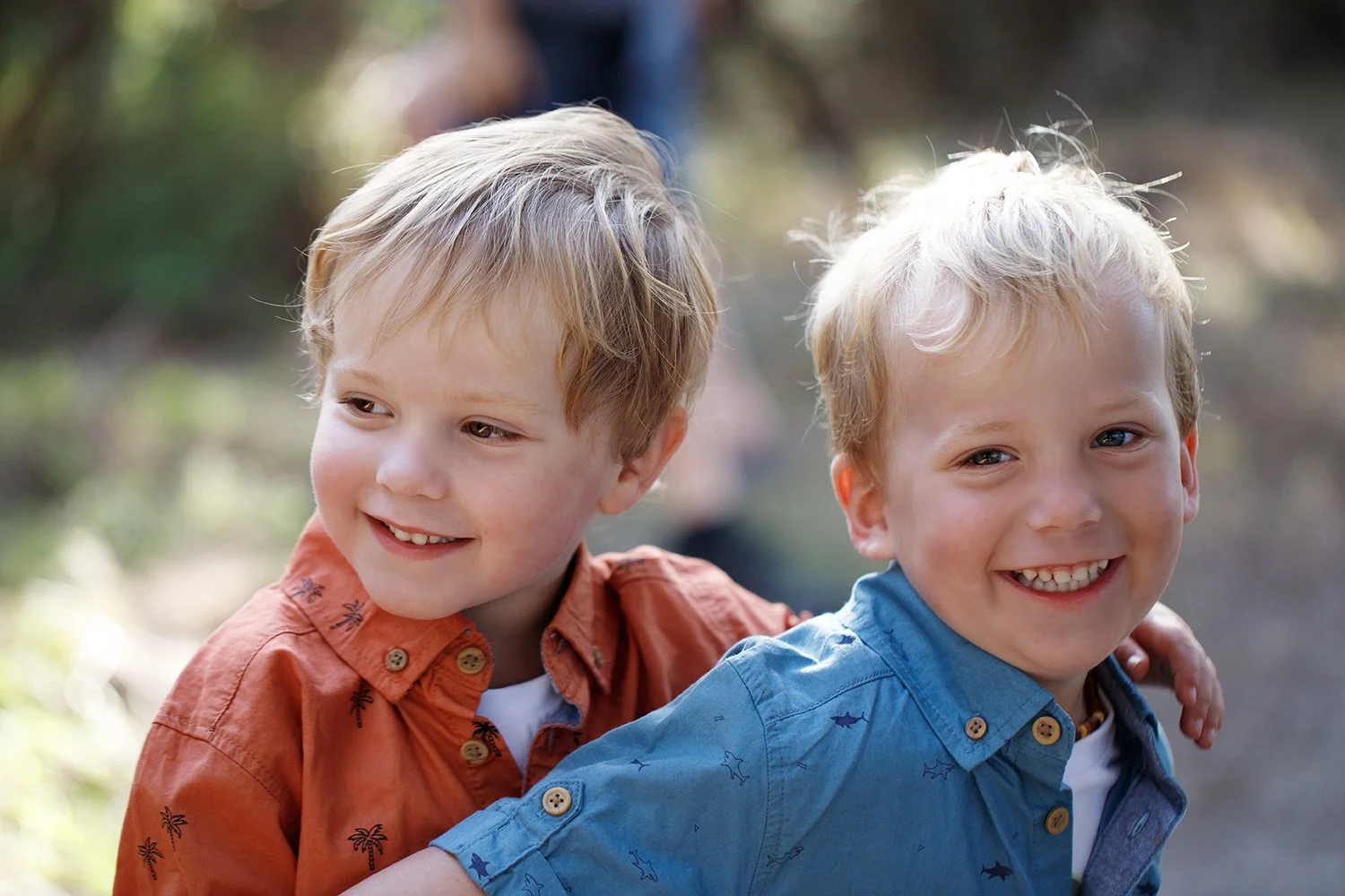 Two young boys outdoors, smiling, with one boy's arm around the other's shoulder.
