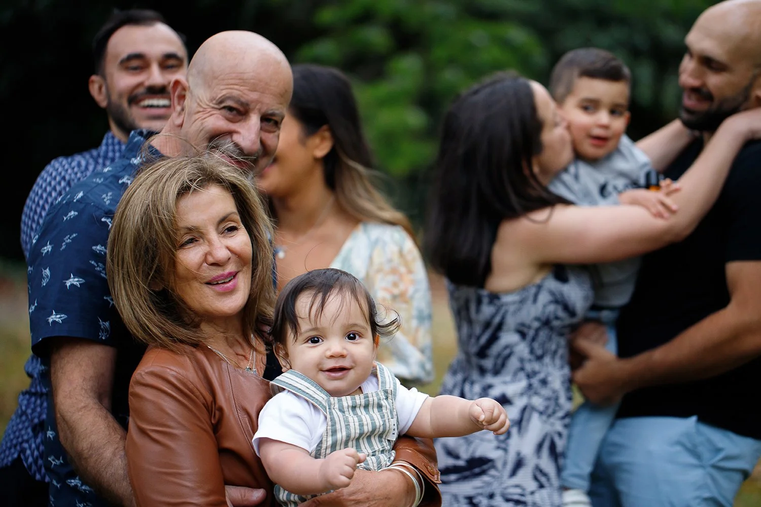 Family group outdoors, including a woman holding a baby, with various adults and children in the background.