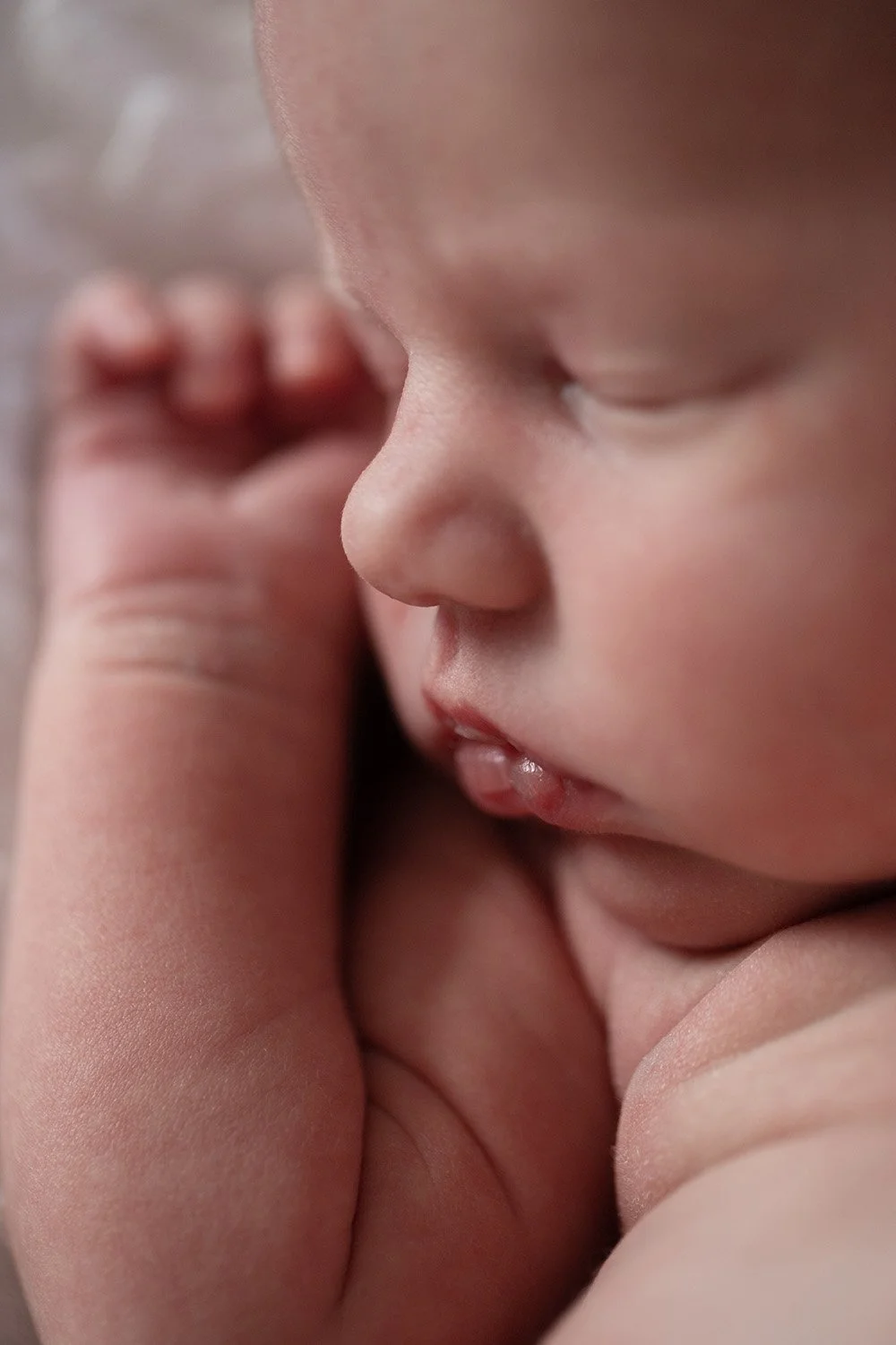 Close-up of a sleeping baby with eyes closed, lying peacefully with hand near face.