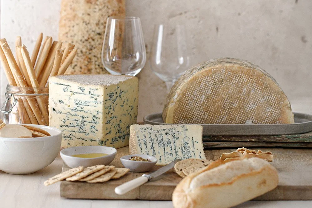 Assorted cheeses, breadsticks, crackers, and glasses of wine on a wooden table.