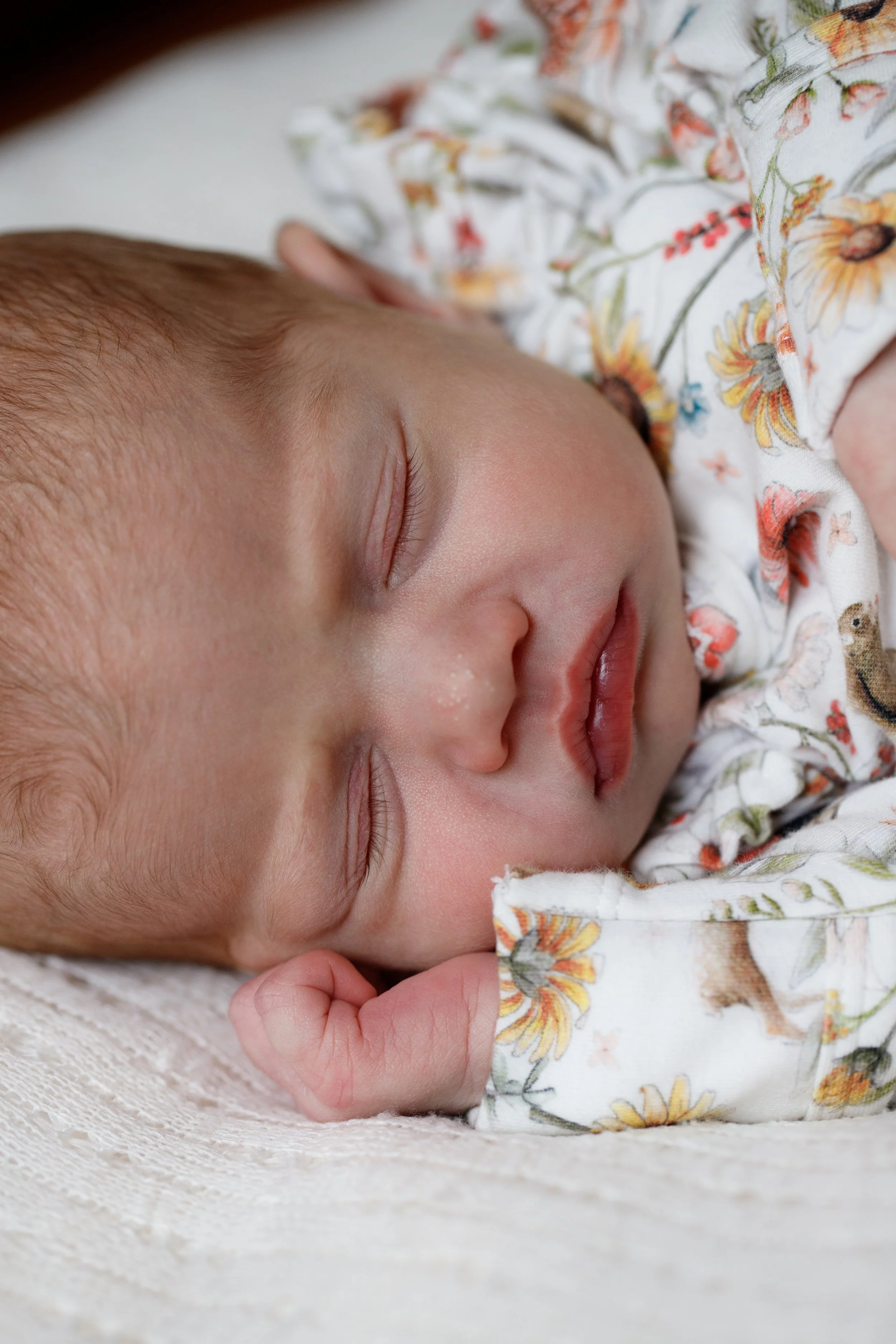 Close-up of a sleeping baby with closed eyes, resting on a soft surface, wearing a floral patterned shirt.