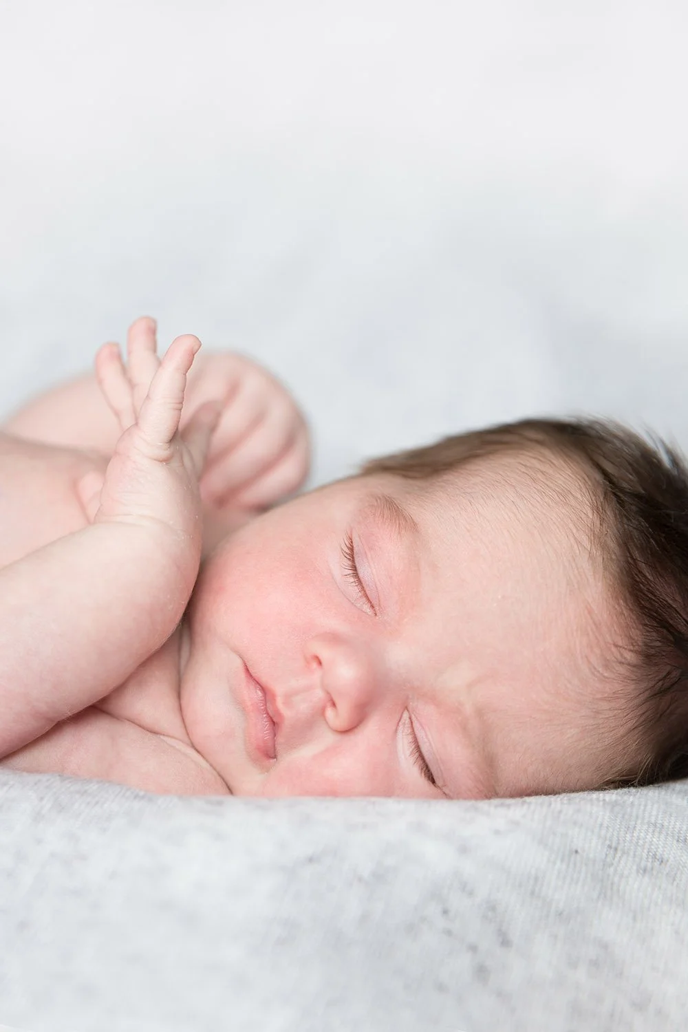 Close-up of a sleeping baby with a gentle hand near their face, lying on a soft surface with a neutral background.
