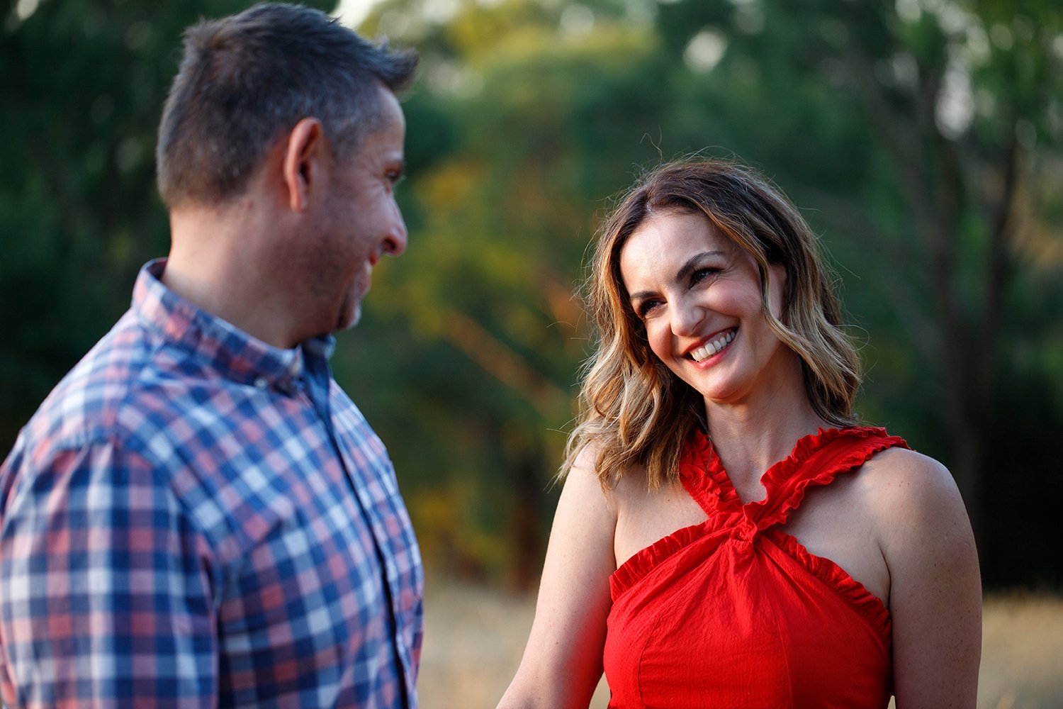 A man and a woman smiling at each other outdoors in a park at sunset