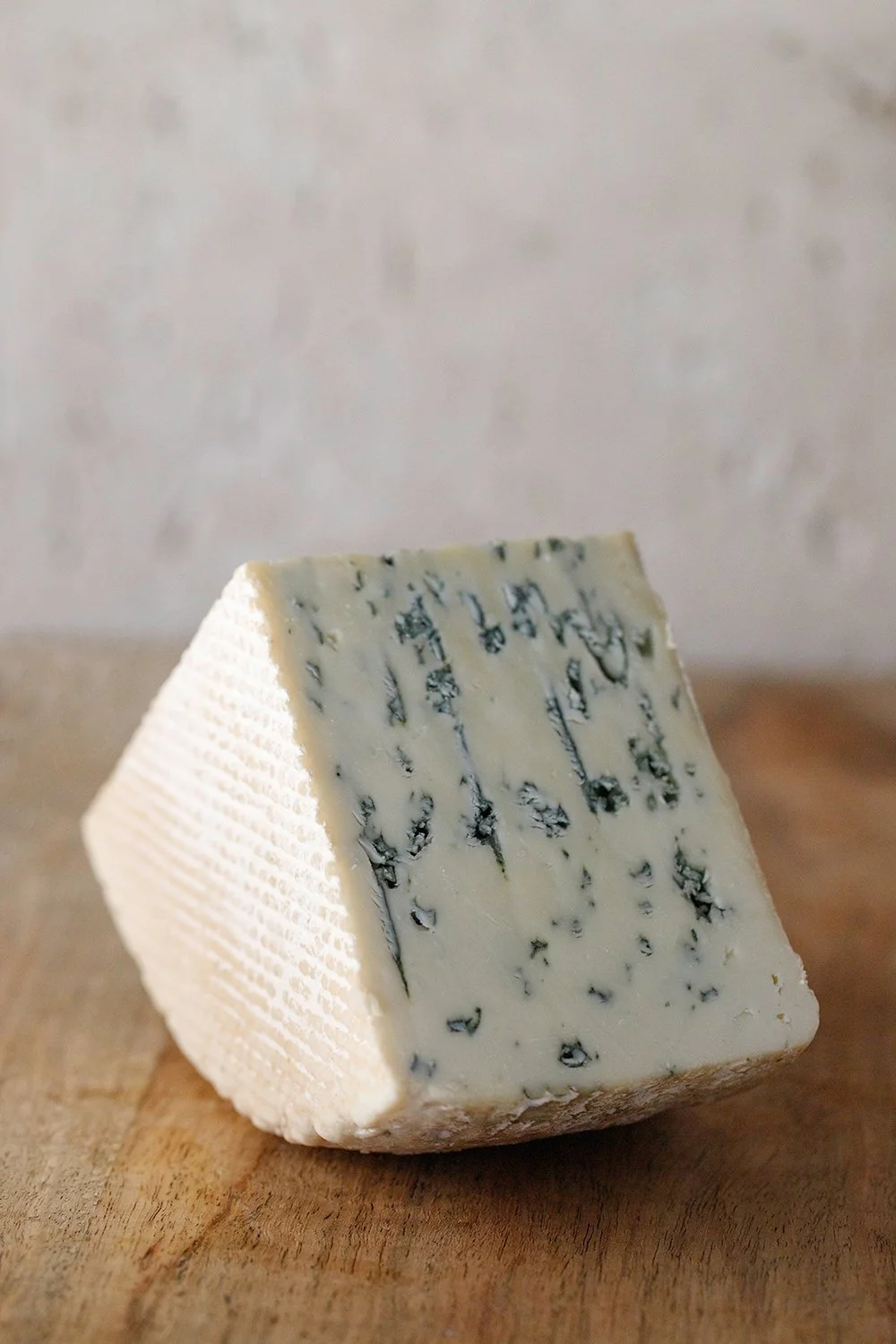 A wedge of blue cheese with blue veins, placed on a wooden surface.