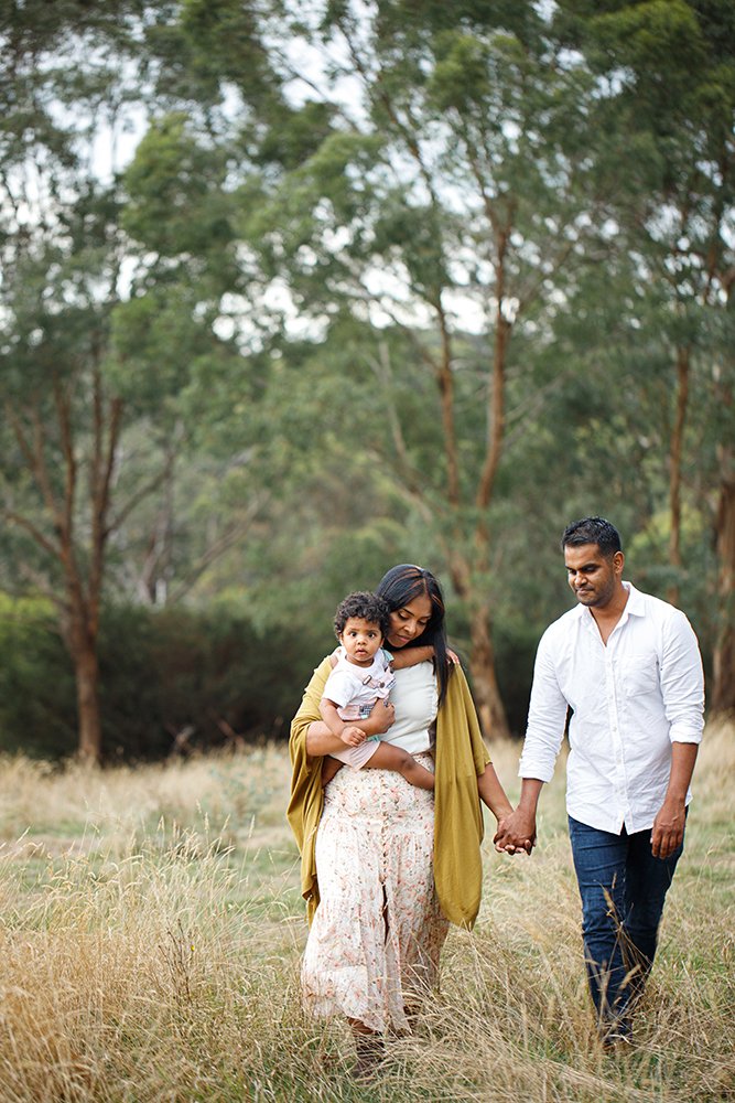 A family walking hand in hand through a grassy field with trees in the background.