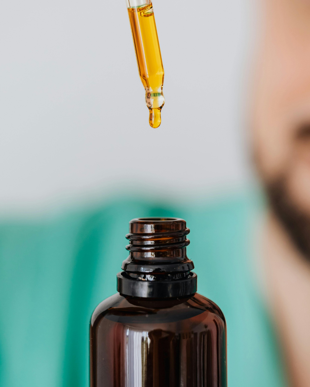 A dropper dispensing golden liquid into a dark amber glass bottle.