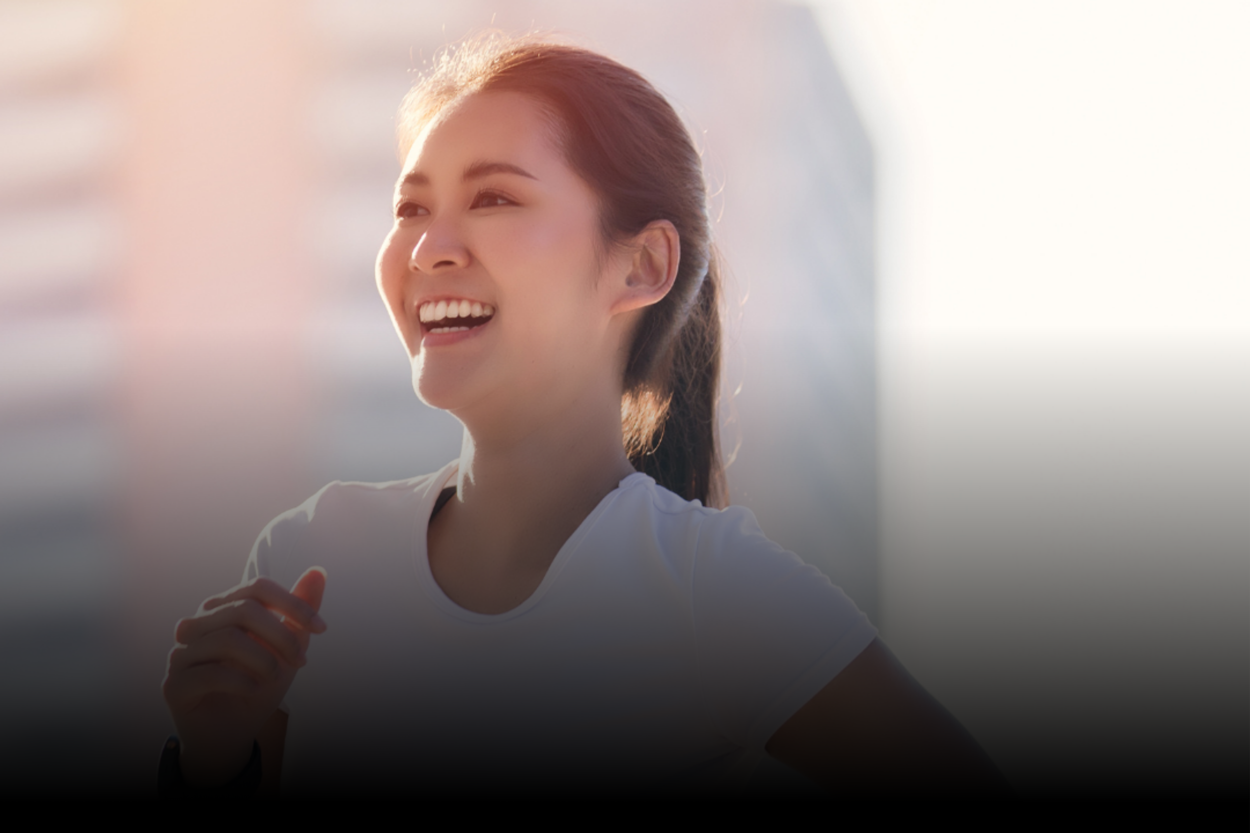 A young woman smiling and running outdoors with sunlight shining on her.