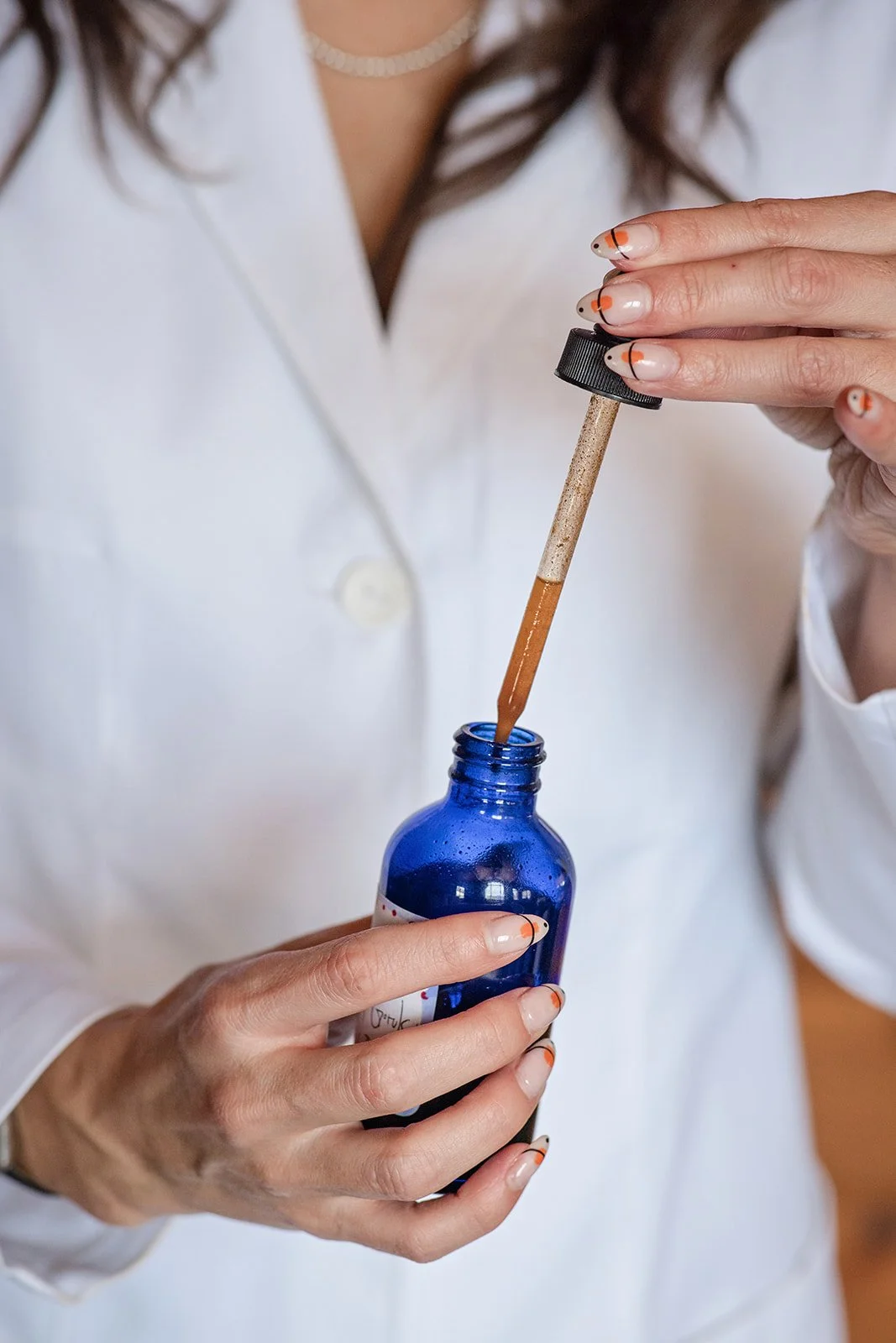 Person in a white lab coat holding a blue bottle with a dropper filled with a brown liquid, used for skincare or cosmetic application.