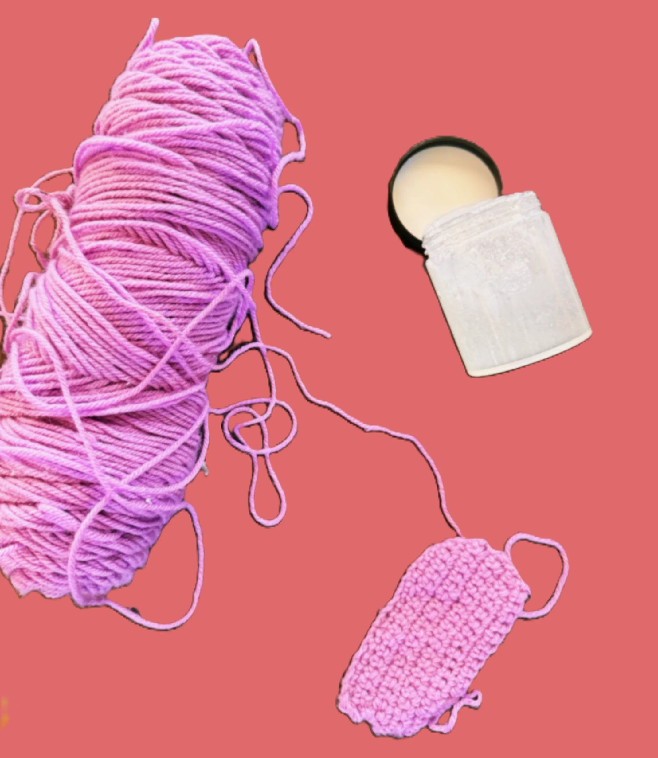 A skein of pink yarn, a partially knitted pink swatch, and a container of white cream lotion are on a pink background.