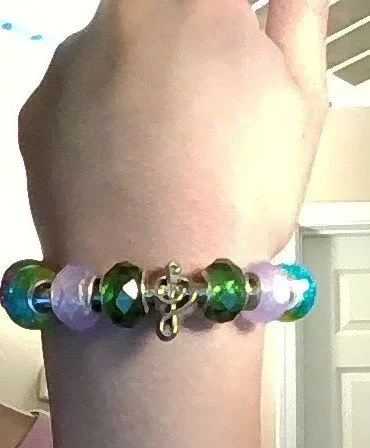 Close-up of a hand wearing a beaded bracelet with multicolored beads and a small anchor charm.