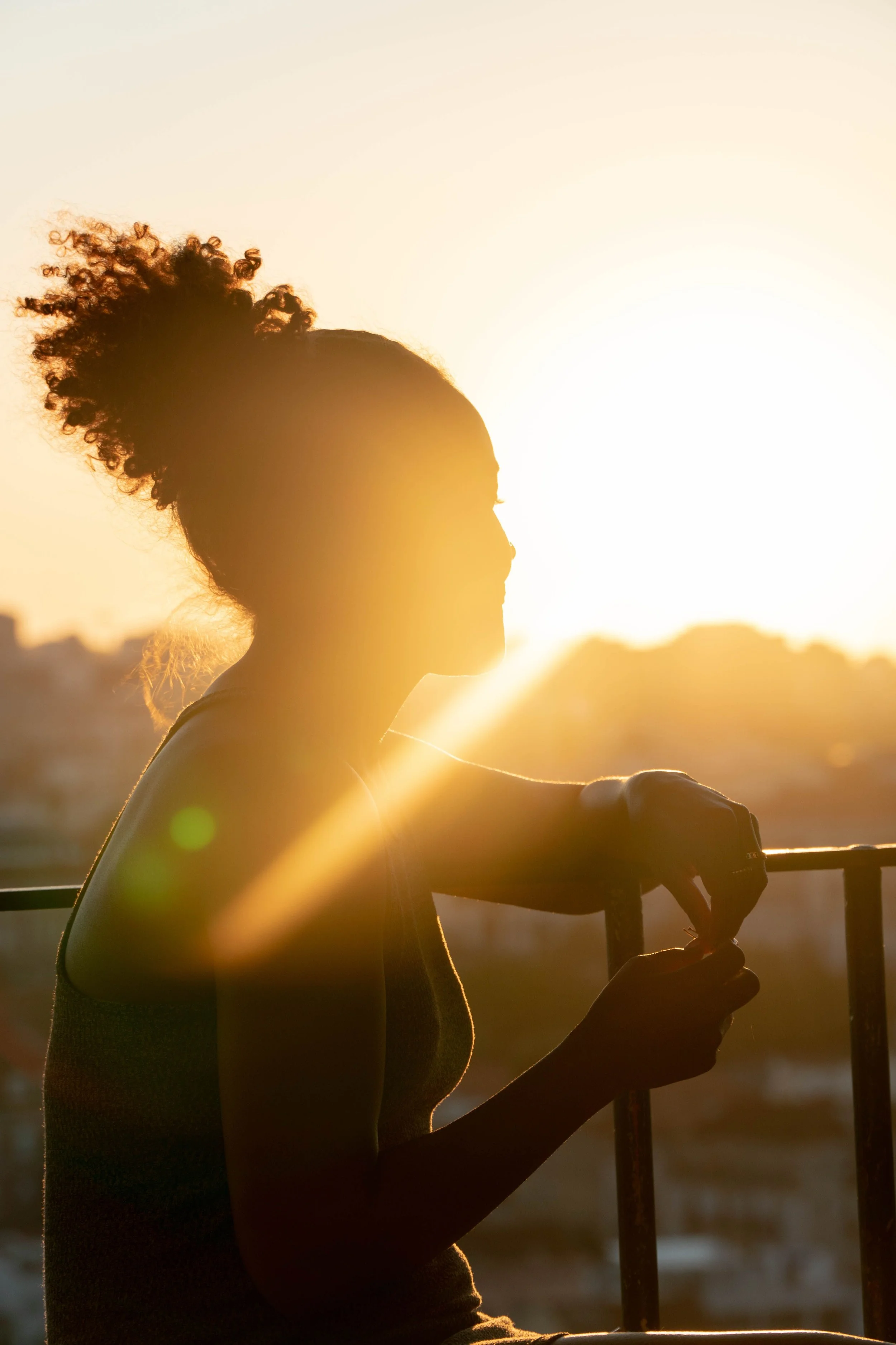 Silhouette d'une femme avec une coiffure bouclée, regardant vers la droite, tenant un bâton, au coucher du soleil.