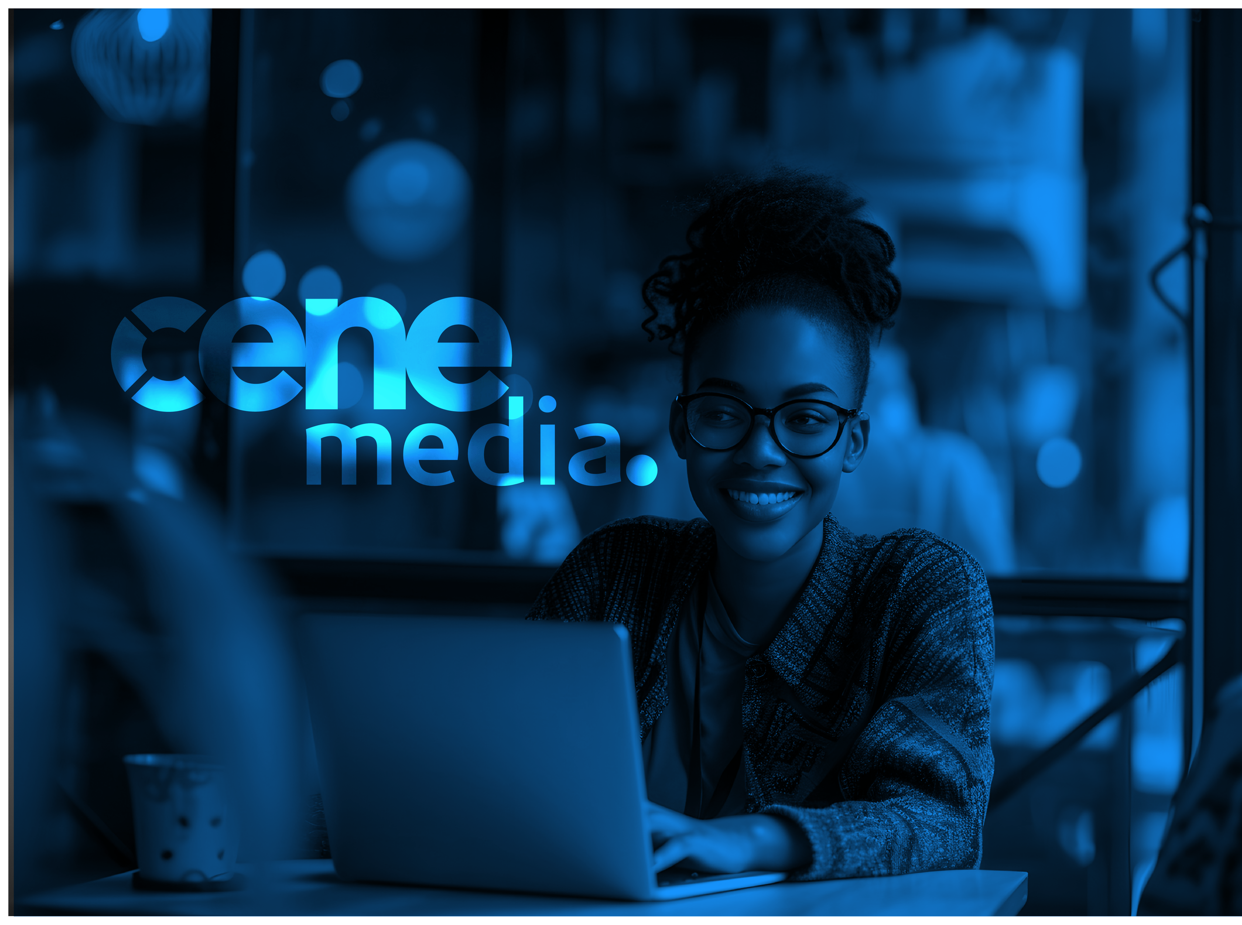 A woman with glasses and curly hair smiling while working on a laptop in a cafe, with a sign in the background that reads 'cena media'.