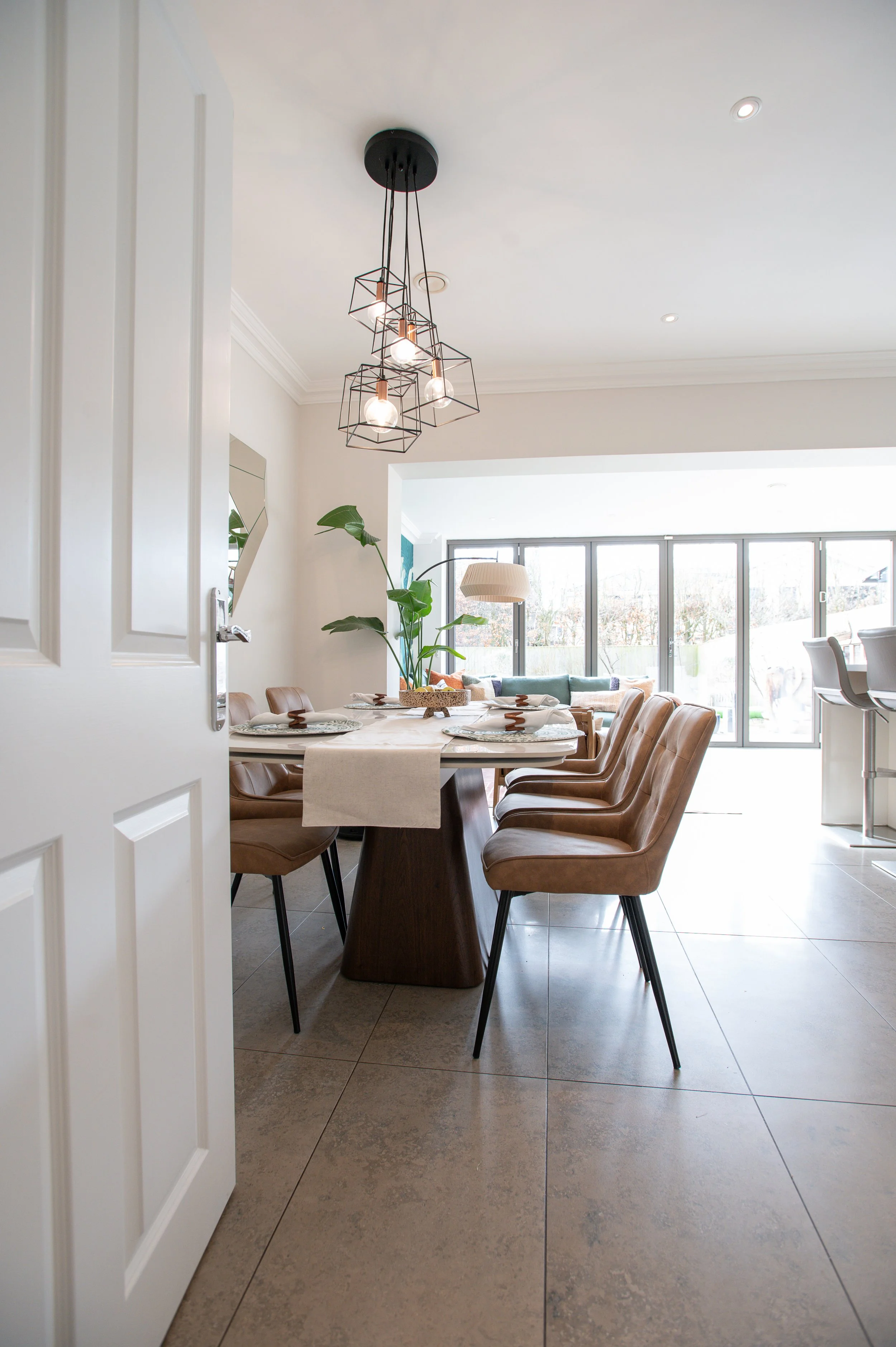 Open plan dining area in a modern Alderley Edge family home featuring warm wood tones, leather dining chairs, layered lighting and contemporary interior design by Studio Dimora.