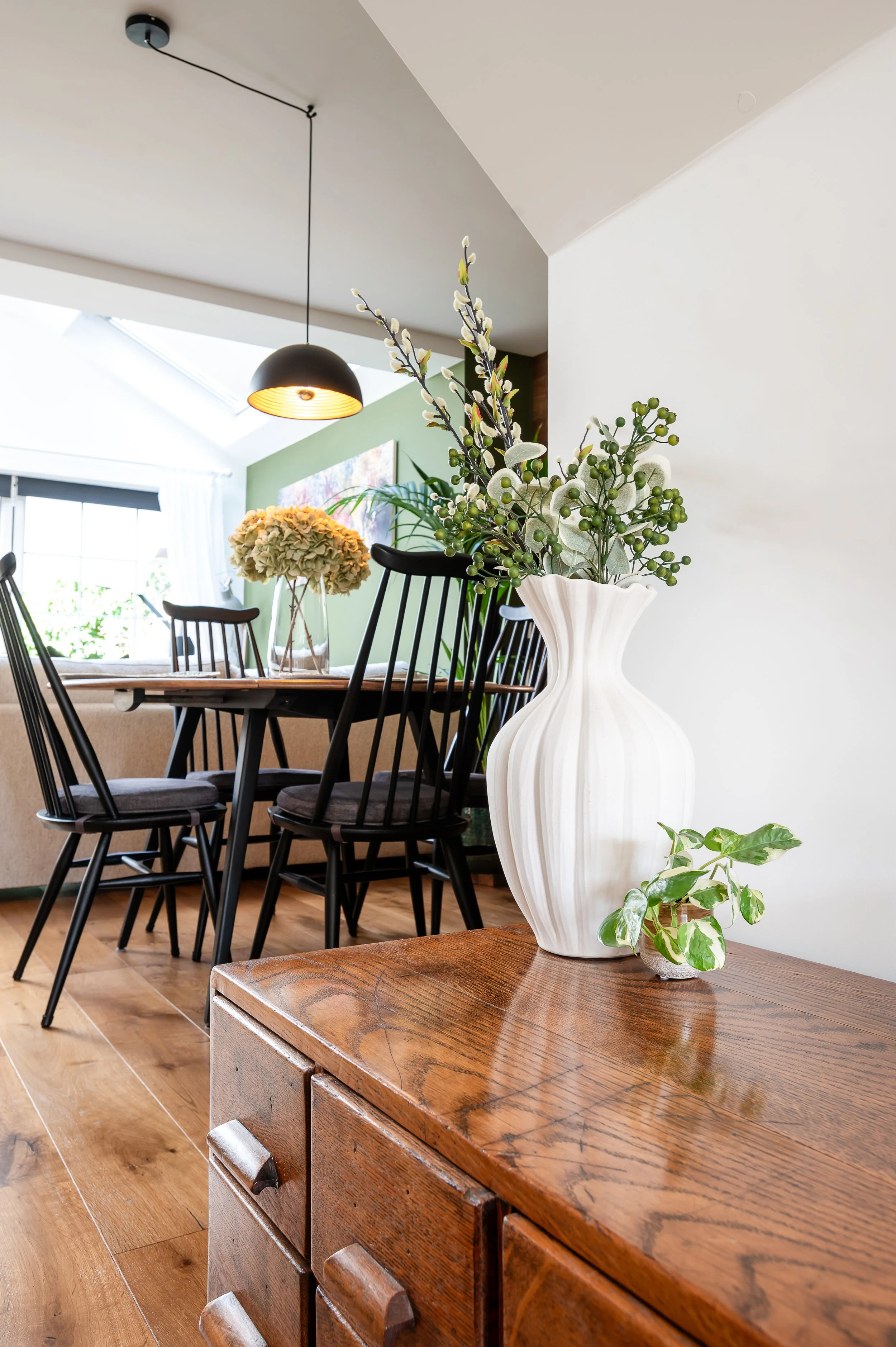 Contemporary dining area in a Wilmslow family home featuring warm wood flooring, black dining chairs, layered lighting and modern organic interior styling by Studio Dimora.
