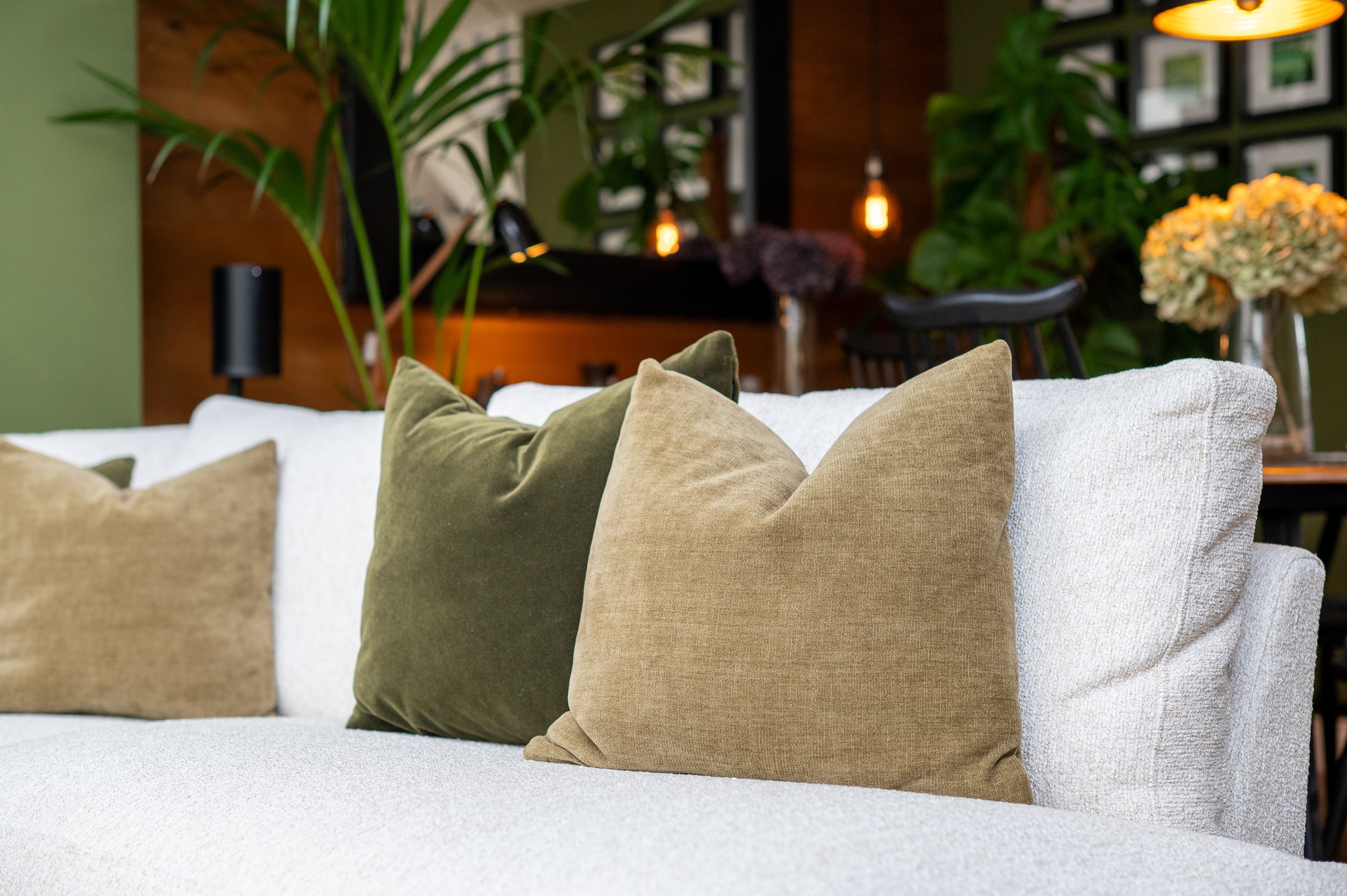 Close-up of a white upholstered sofa with olive green and neutral cushions in a warm, contemporary interior.