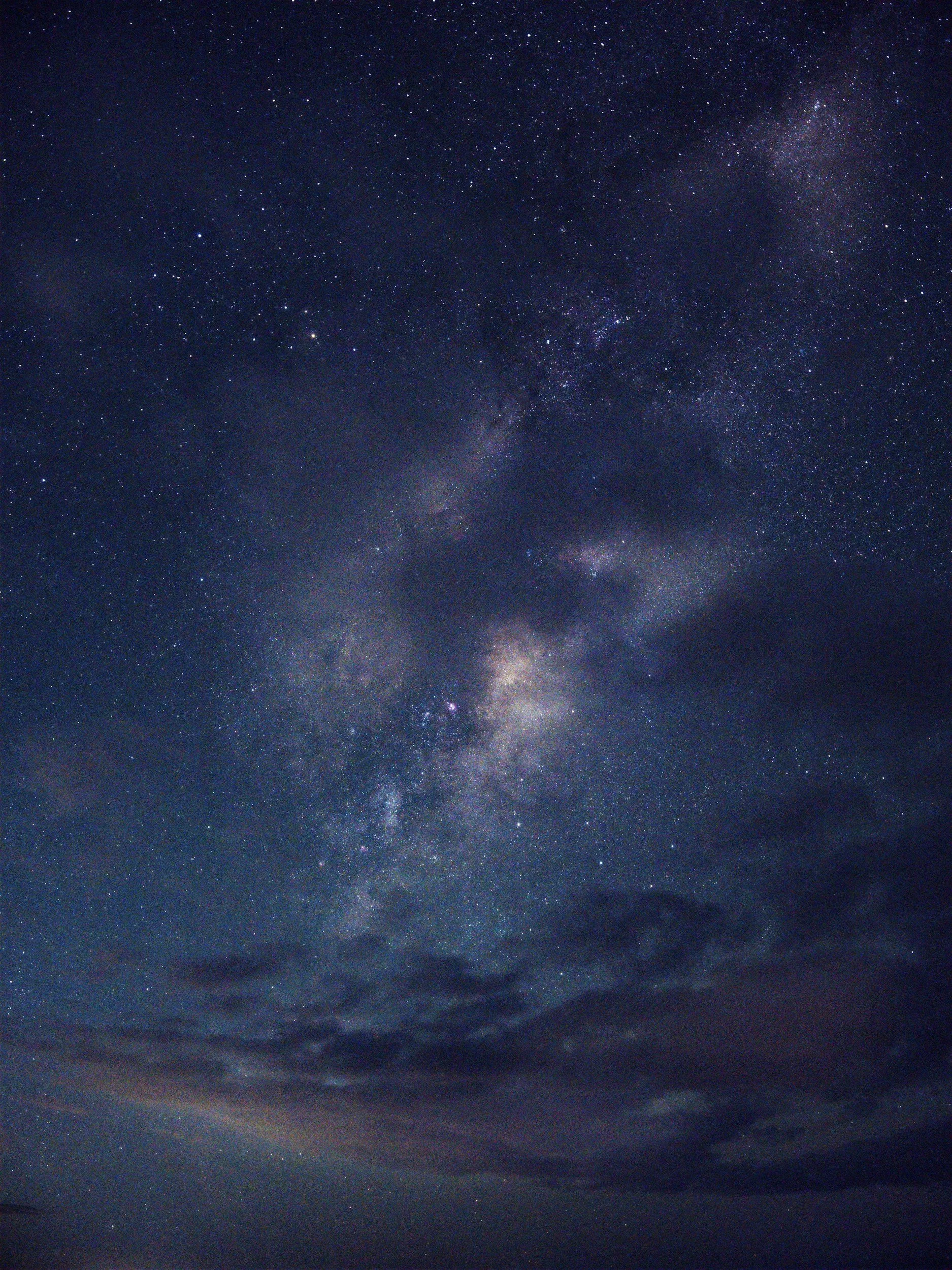 Night sky filled with stars and the Milky Way galaxy, with some clouds at the bottom.