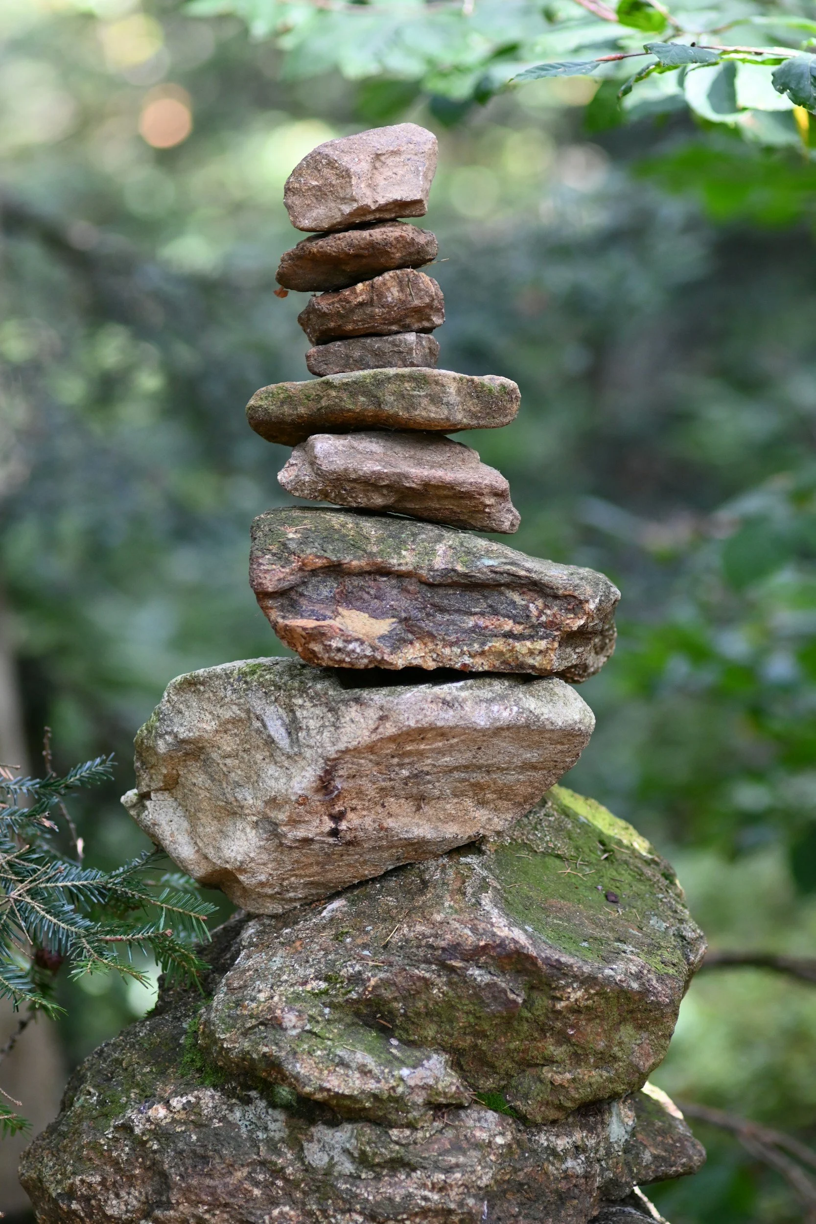 Stacked rocks balanced on top of each other in a natural outdoor setting with blurred green foliage in the background.