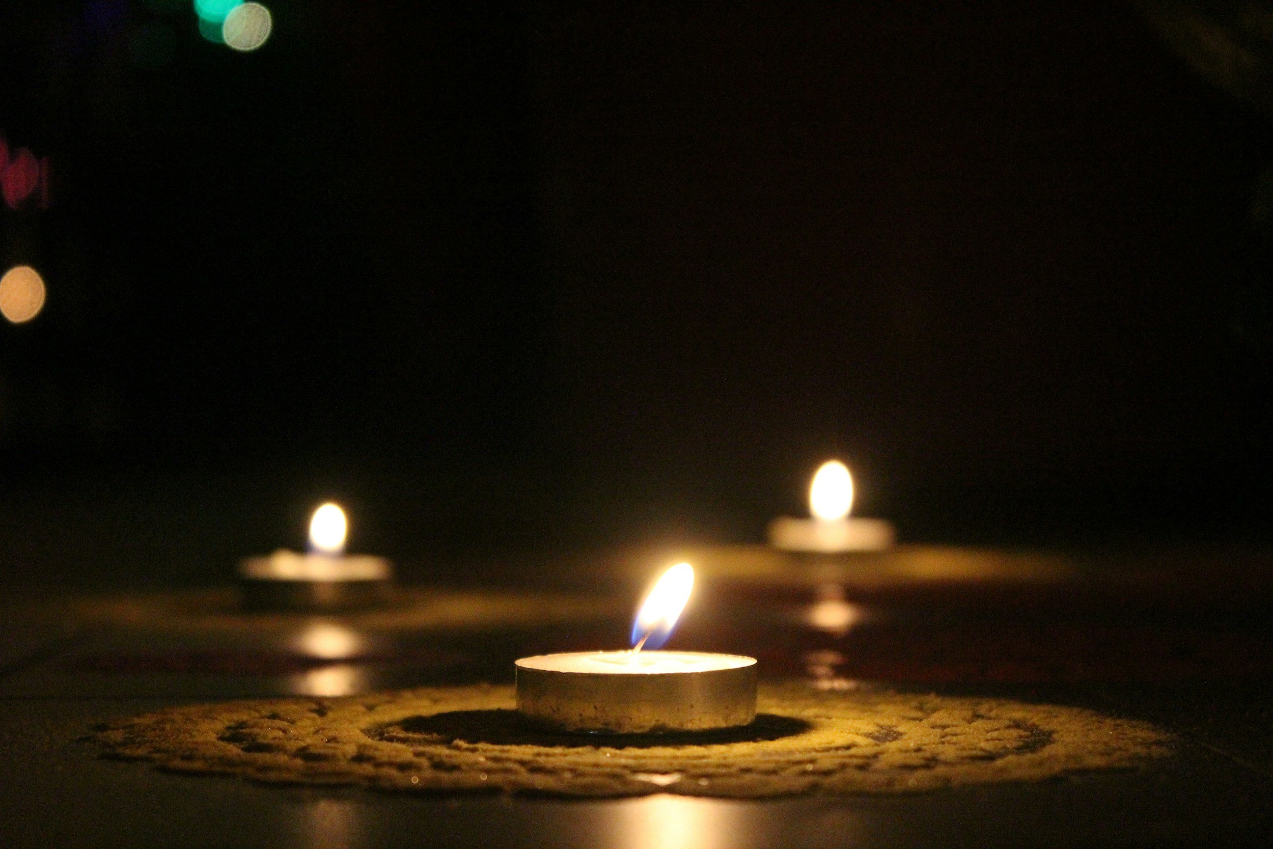 Three lit tea light candles on a dark surface, creating a soft, warm glow.