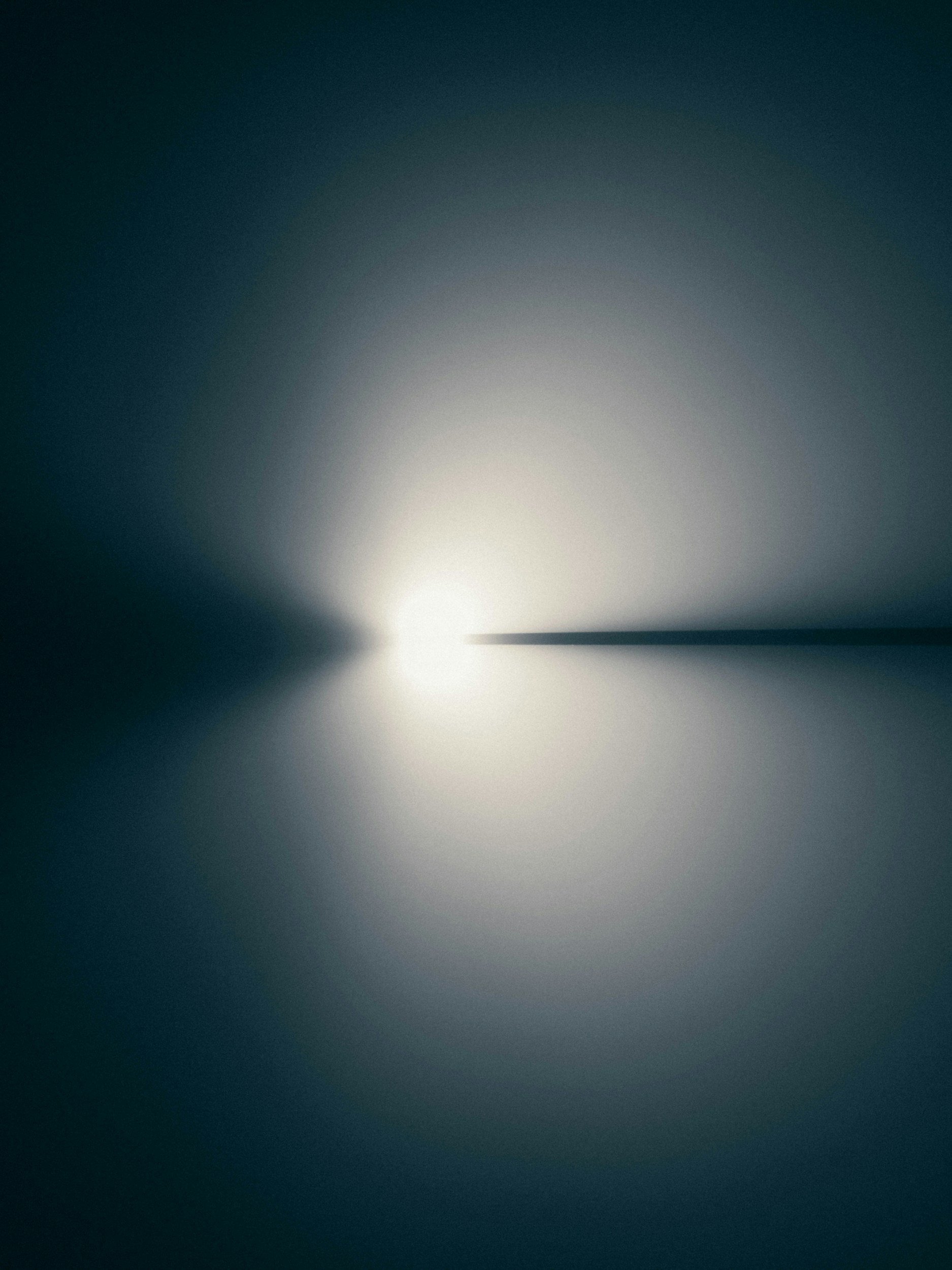 Abstract image with a bright light source at the center, creating a glow and symmetrical gradient of dark blue and gray tones surrounding it.