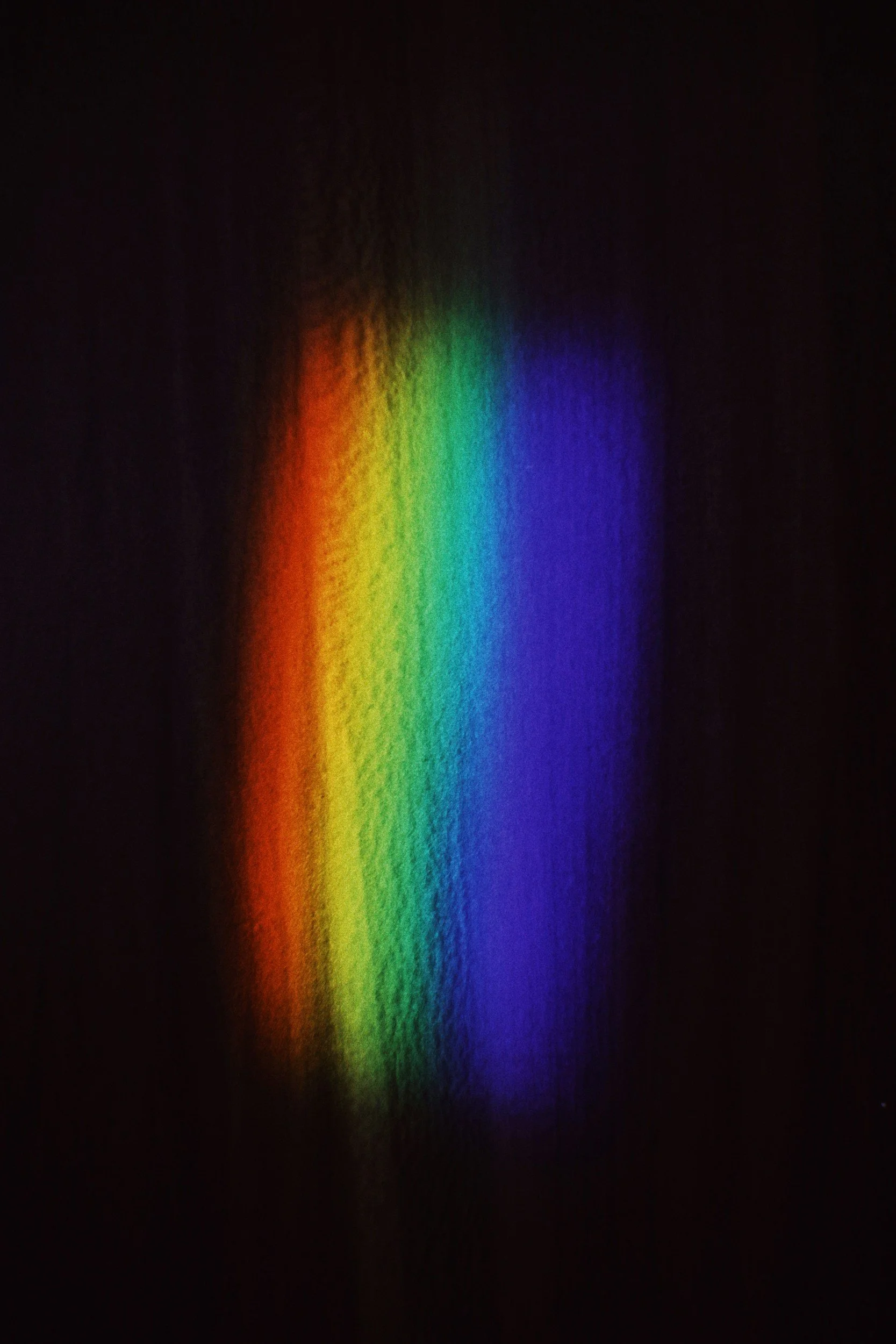 Colorful light projection on a dark wall creating a rainbow pattern.