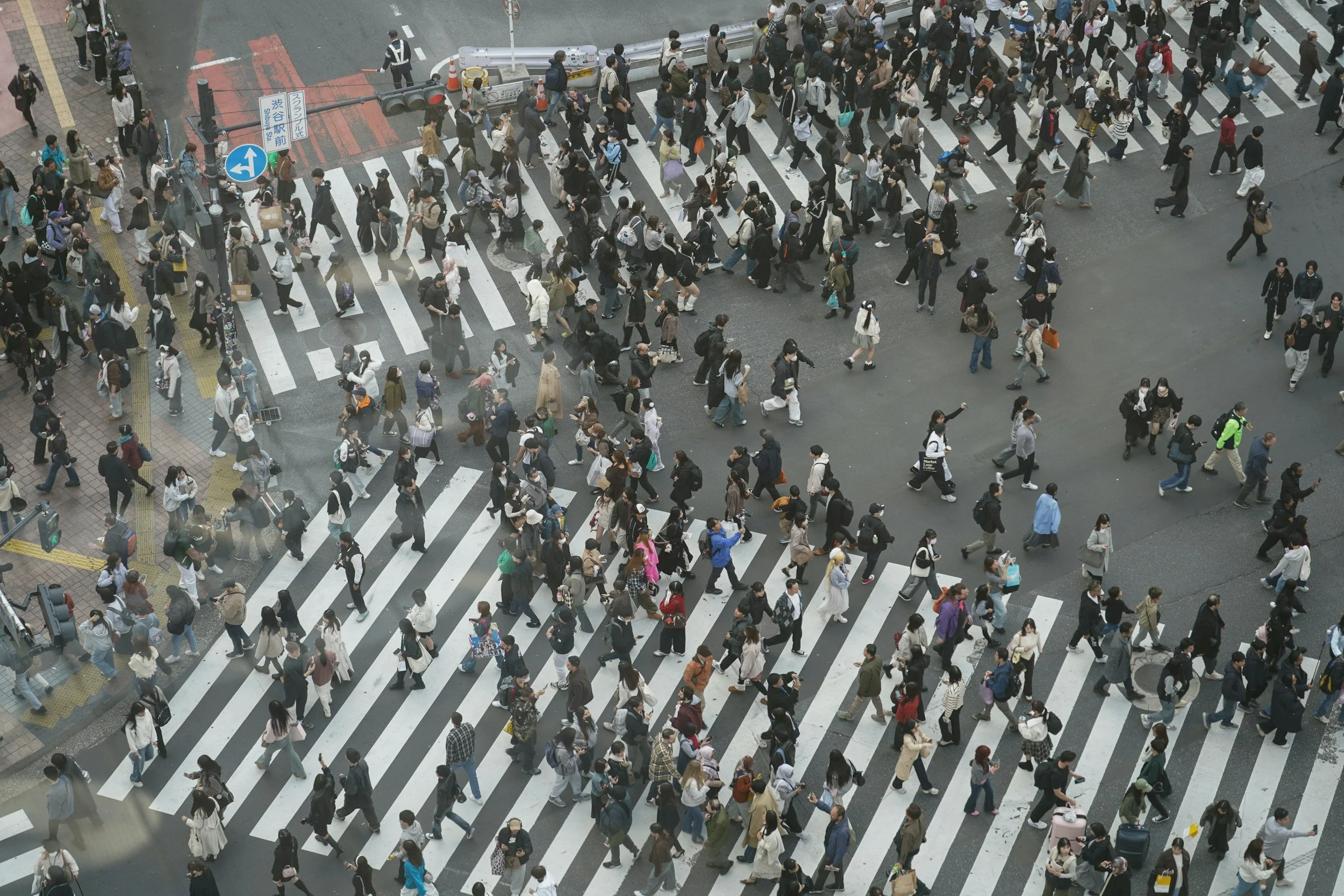 Aerial view of a busy urban crosswalk filled with pedestrians crossing at different times and directions.