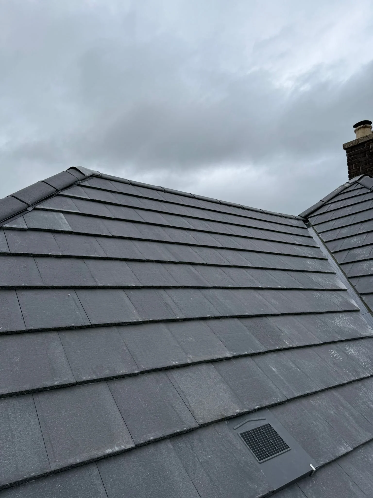 Gray tiled roof with a vent, under a cloudy sky.
