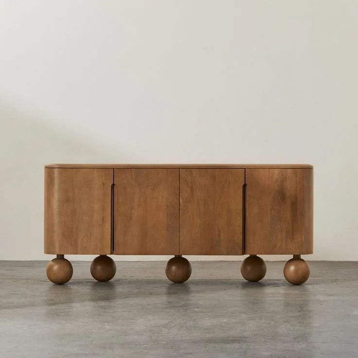 A wooden sideboard with rounded legs against a plain white wall.