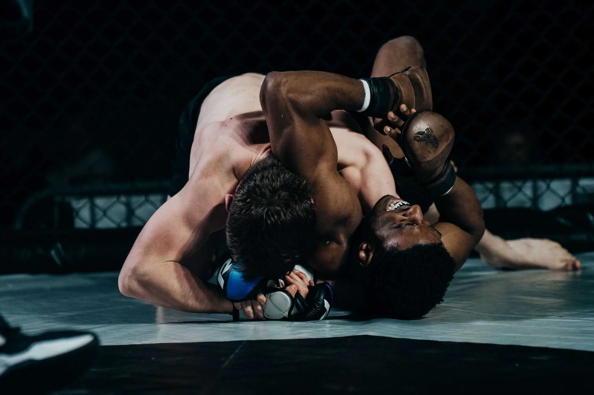 Two mixed martial arts fighters grappling on the mat during a match, with one fighter on top of the other in a rear mount position.