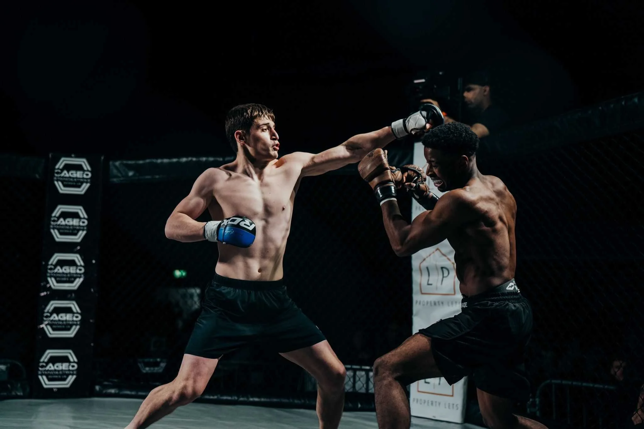 Two mixed martial arts fighters sparring inside a cage, with one delivering a punch to the other's face, during a match.