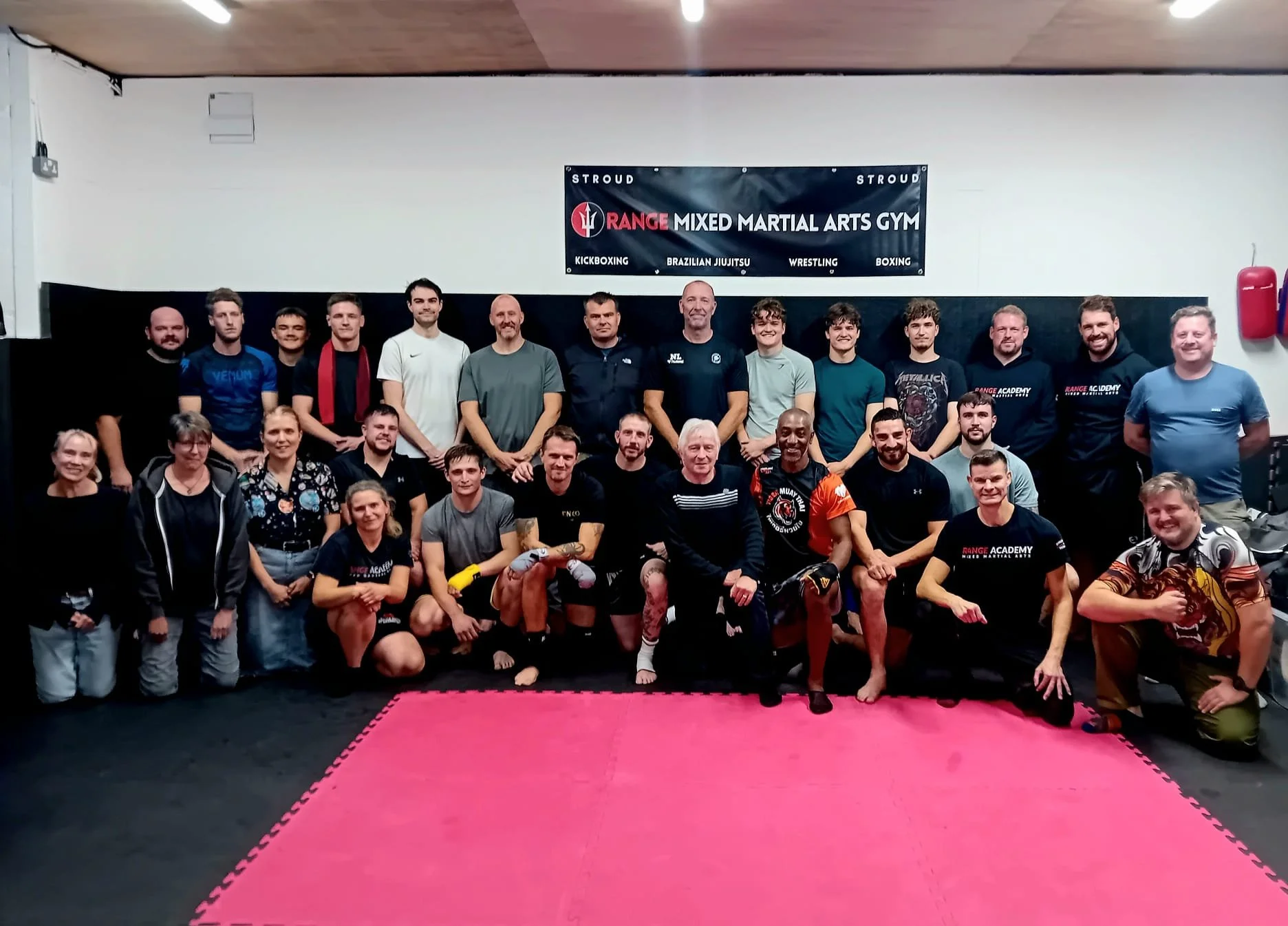 Group photo of martial arts students and instructors at a gym, with a black and white banner reading 'Range Mixed Martial Arts Gym' in the background.