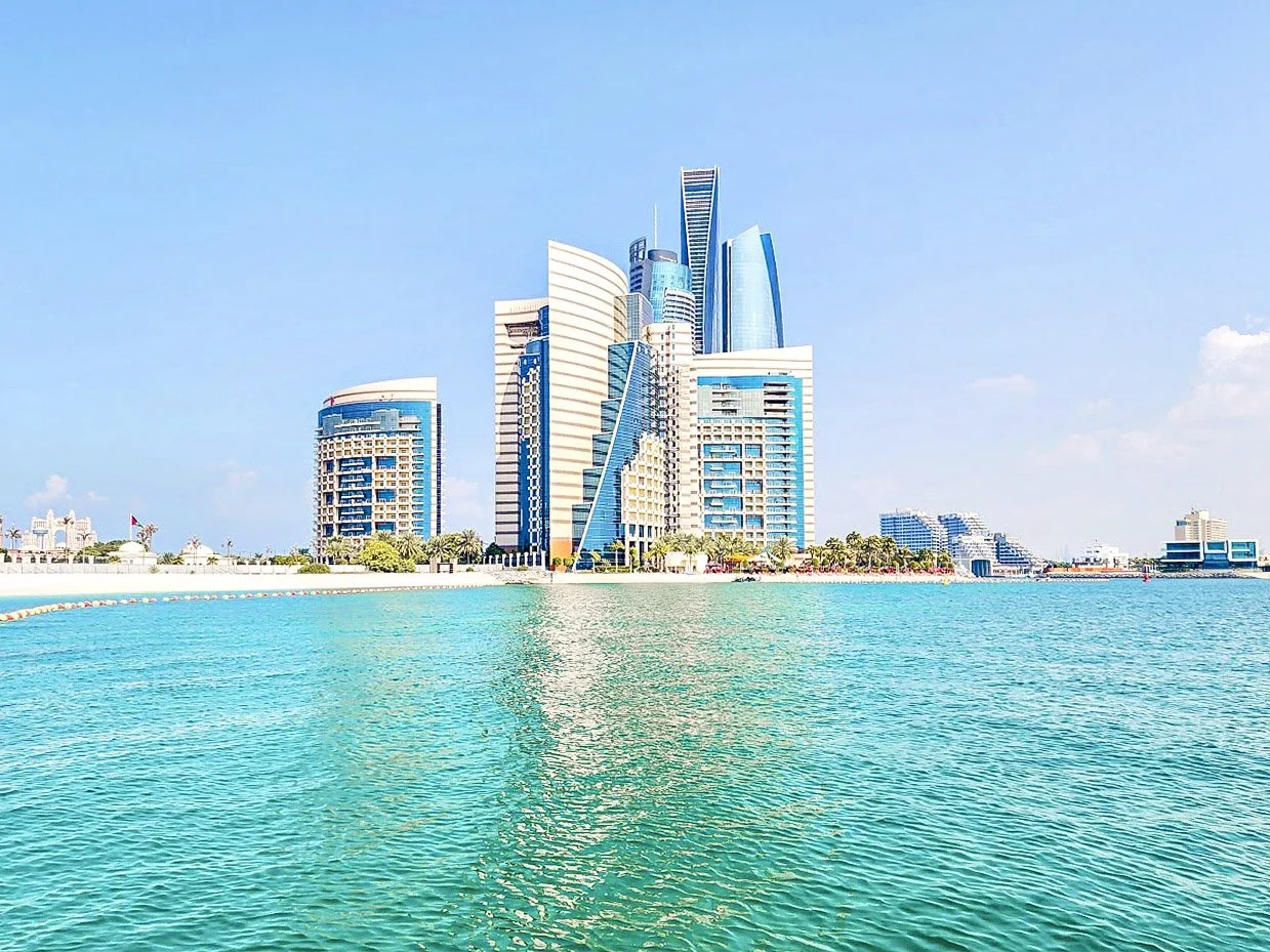 Un ensemble de gratte-ciel modernes à Dubaï, vus depuis la mer, avec un ciel bleu clair.