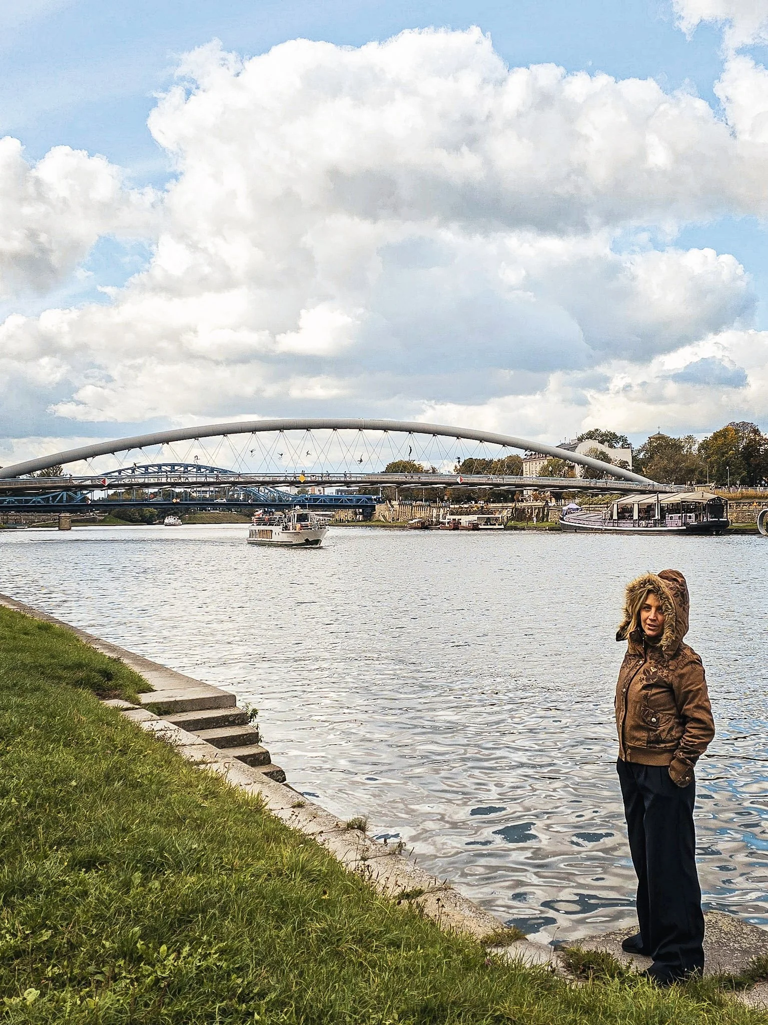 Une personne debout au bord de la rivière, portant une veste marron avec une capuche en fourrure.